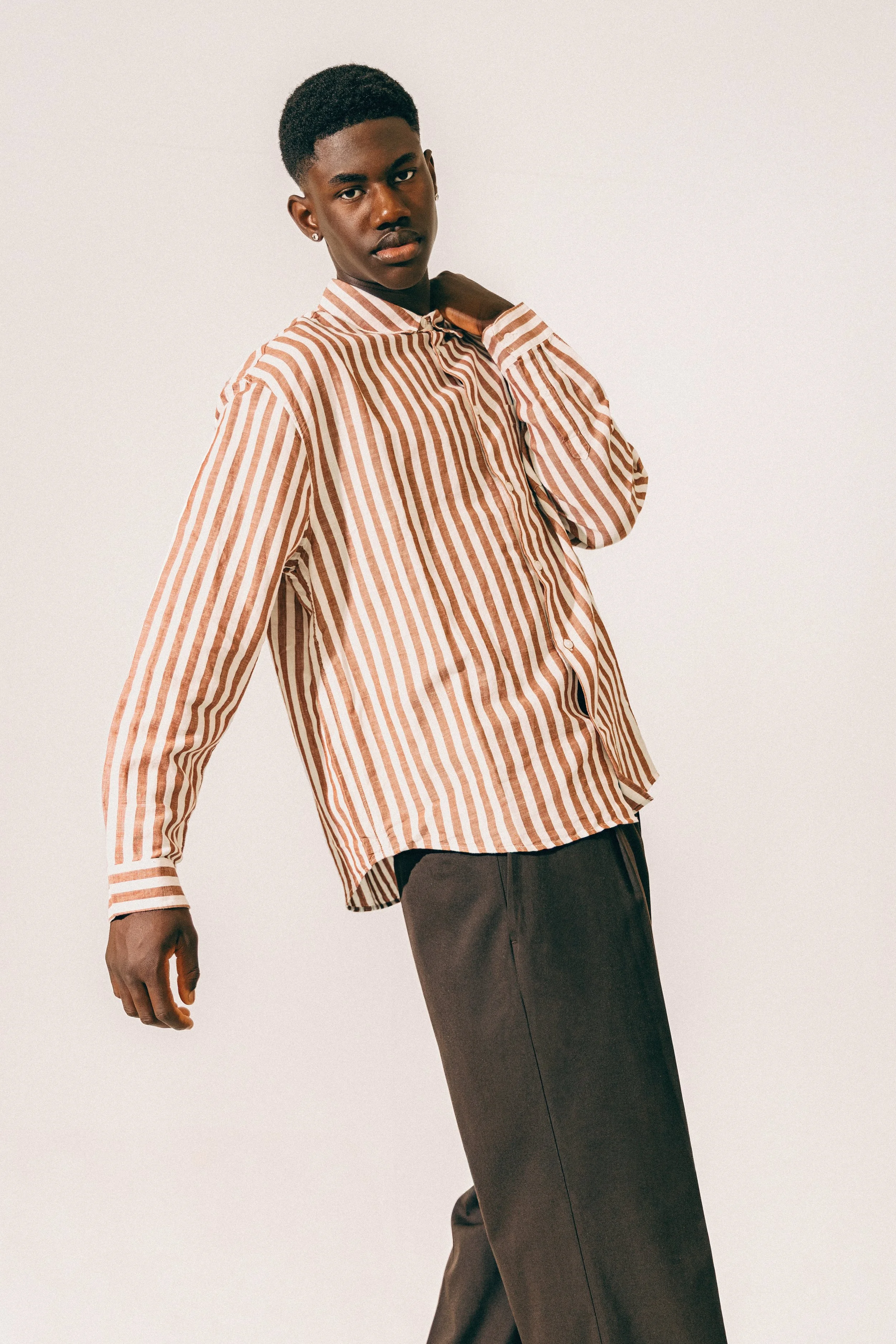 A model wearing a striped, button-up shirt and dark trousers against a plain background.
