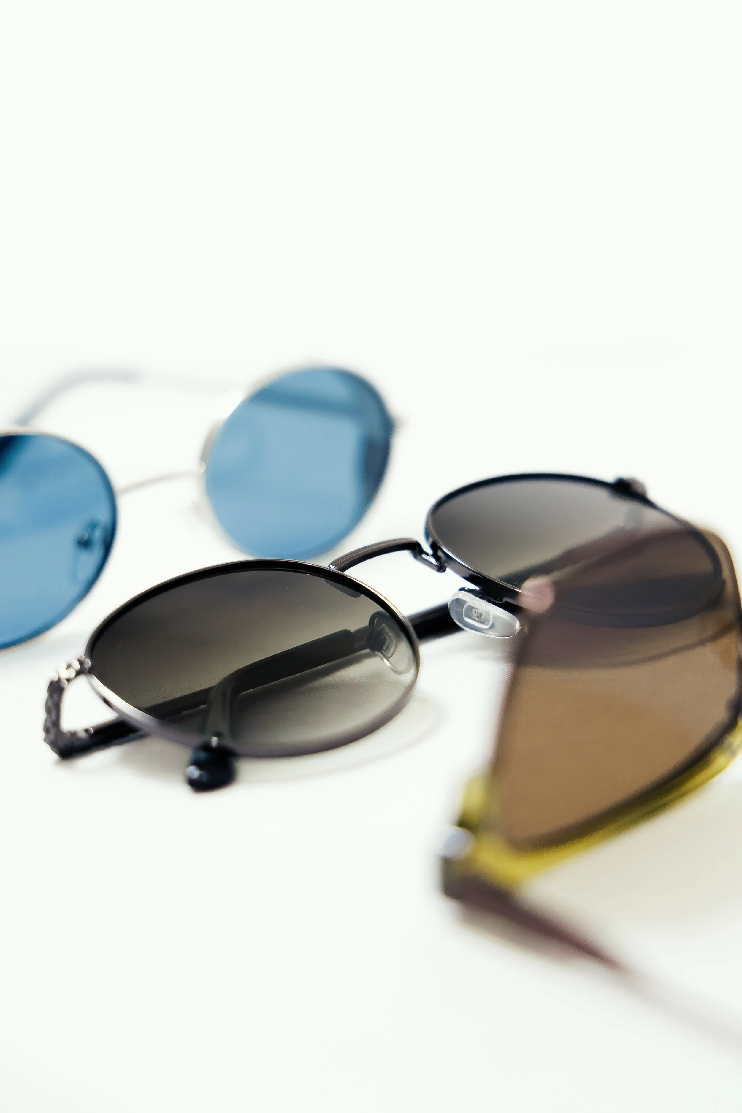 Three pairs of sunglasses with different tinted lenses, arranged on a white surface.