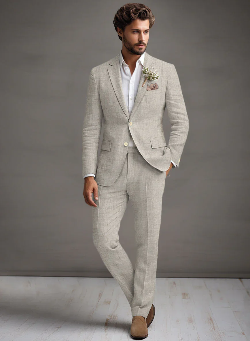 Man wearing a light-colored suit with a white shirt and brown shoes, standing against a plain background.