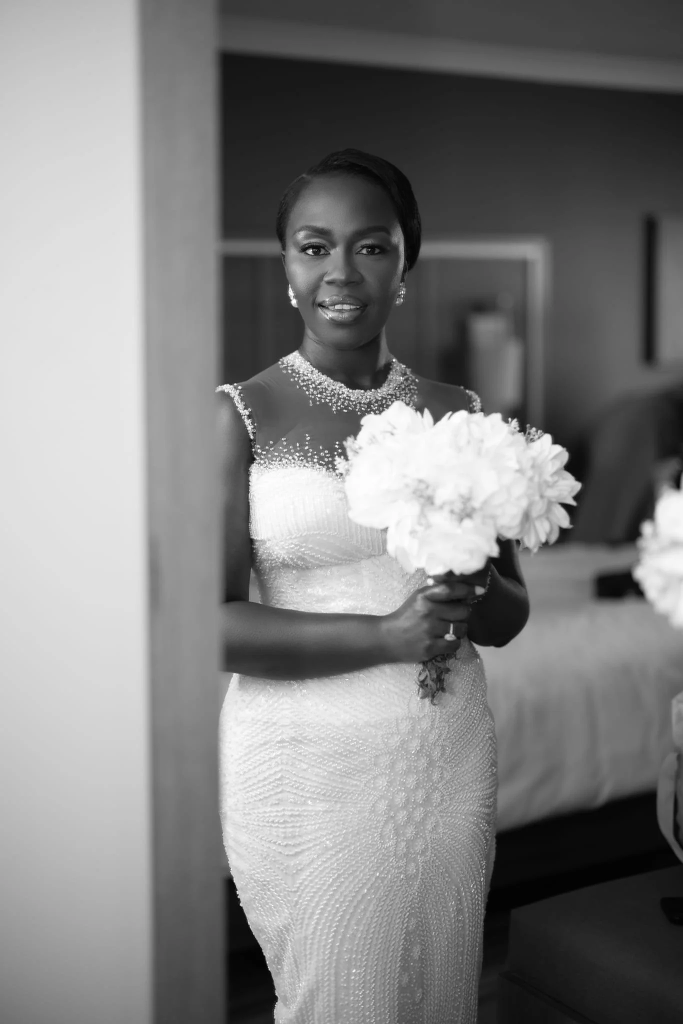 A woman in a wedding dress holding a bouquet of flowers, standing indoors.