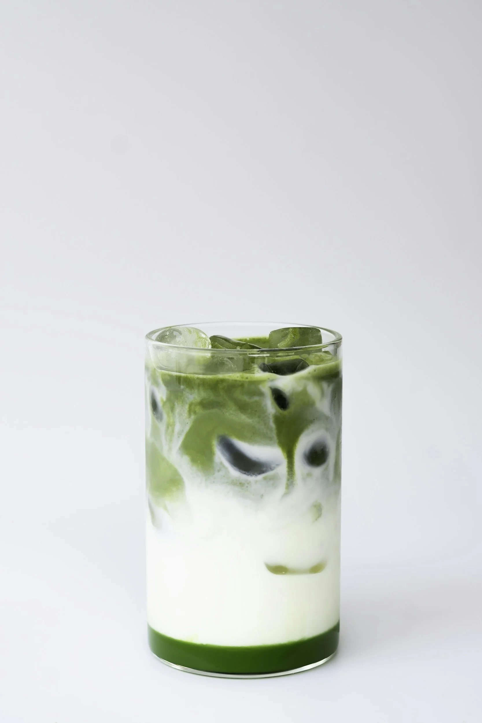 Glass of iced matcha latte with swirling green and white layers, on a white background.