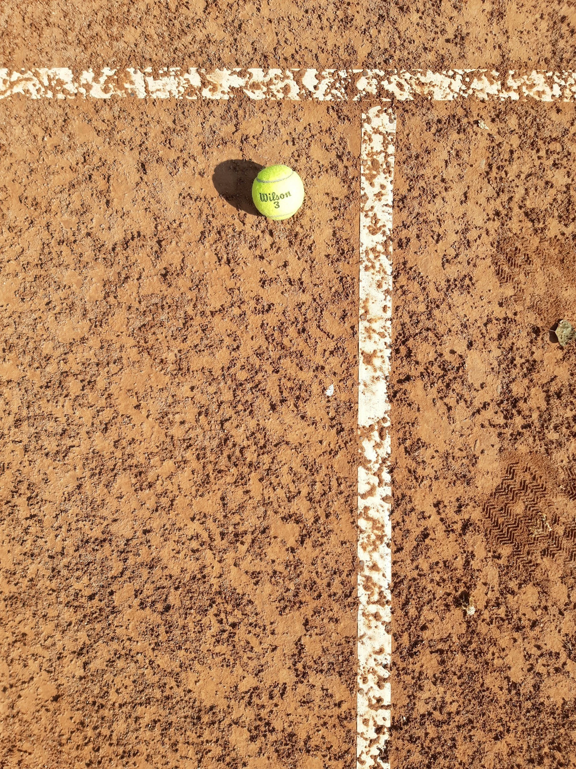 Une balle de tennis sur un terrain de tennis en terre battue, près d'une ligne blanche