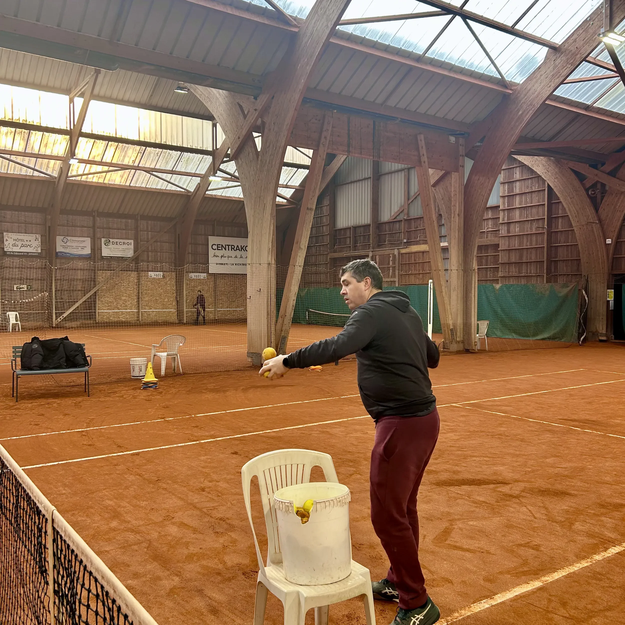 Homme qui s'entraîne avec un ballon de tennis dans un court de tennis intérieur en terre battue.