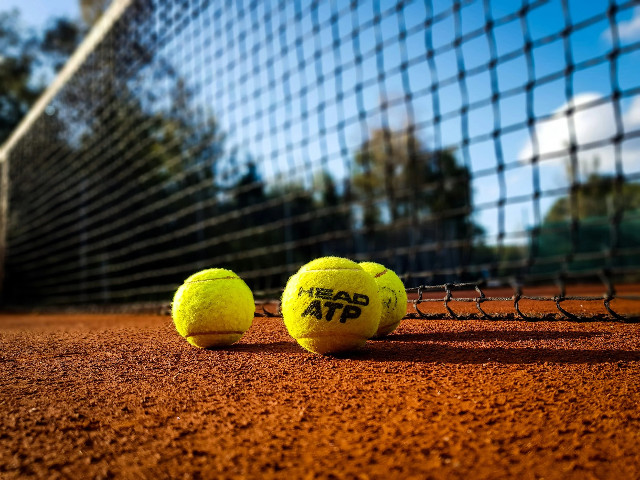 Quatre balles de tennis jaunes sur un court de tennis en terre battue avec un filet en arrière-plan.