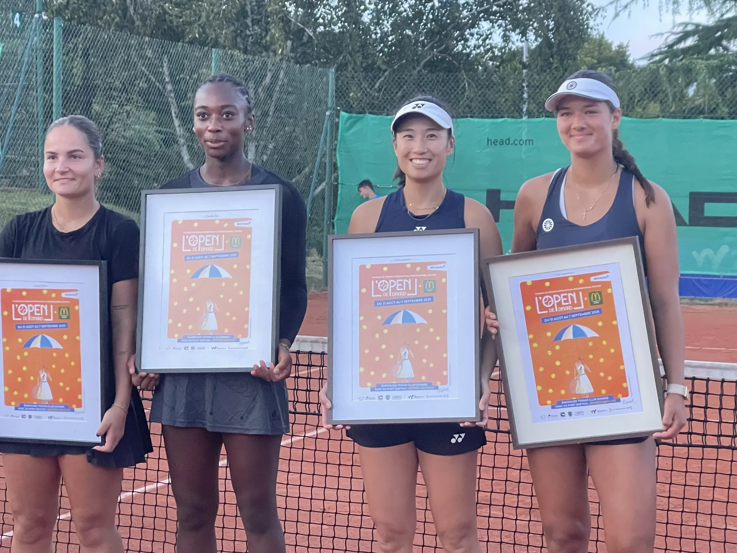 Quatre femmes tennis tenant des posters lors d'une remise de prix sur un court de tennis en extérieur.