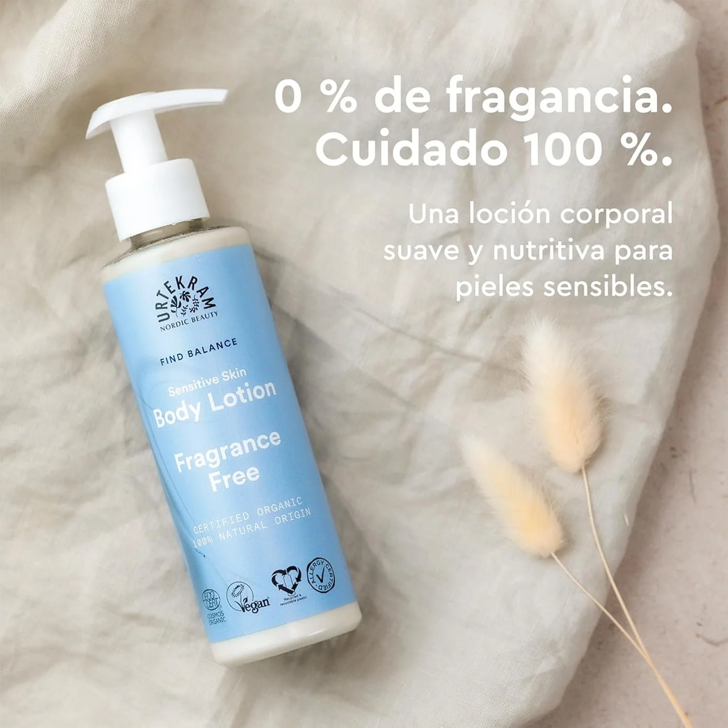 Botella de loción corporal en envase blanco con etiqueta azul y texto, ubicada sobre tela beige, acompañada de plantas decorativas de color crema flacas.