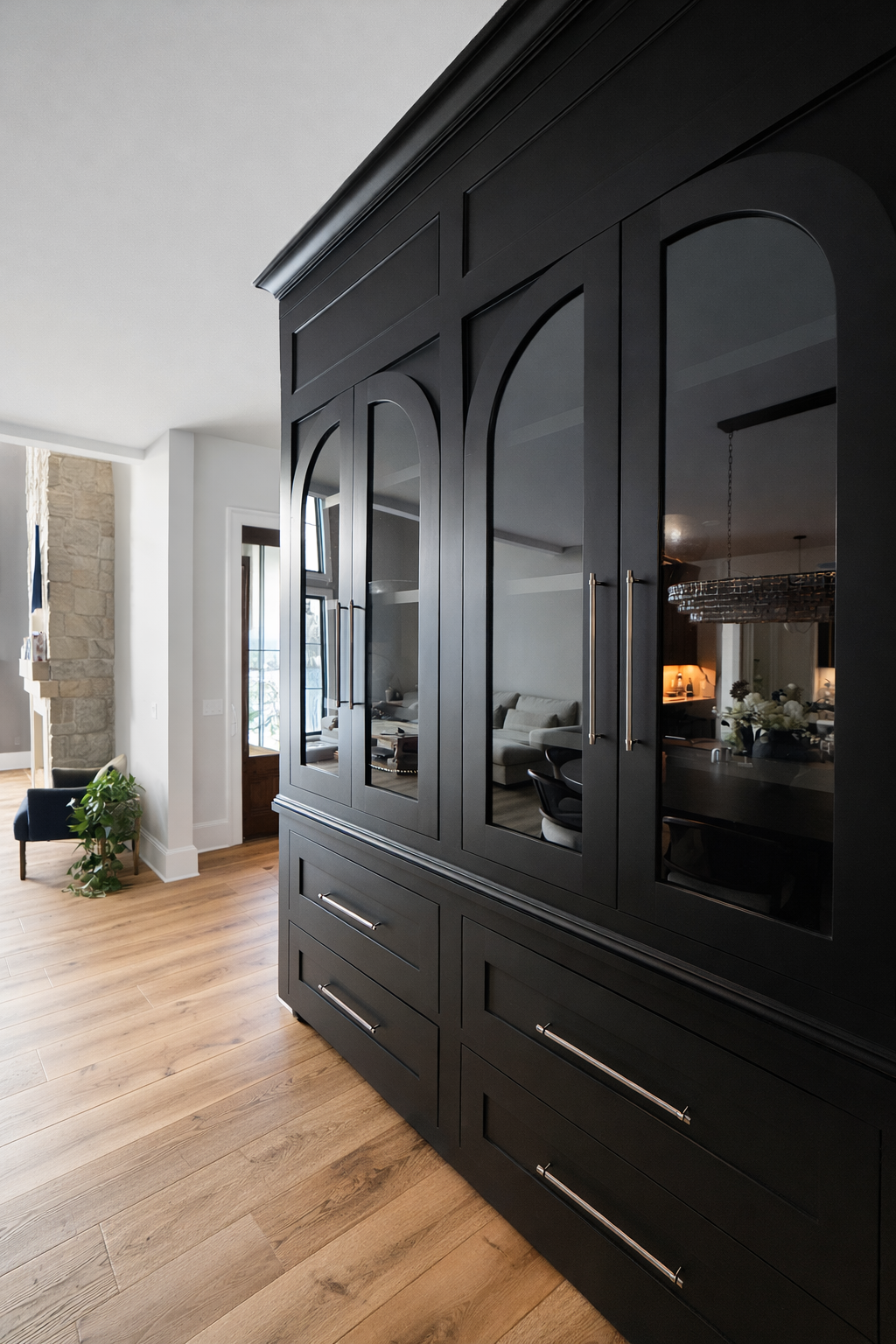 Black built-in cabinet with glass doors in a modern interior, reflecting a living room with a white couch and decorative items.