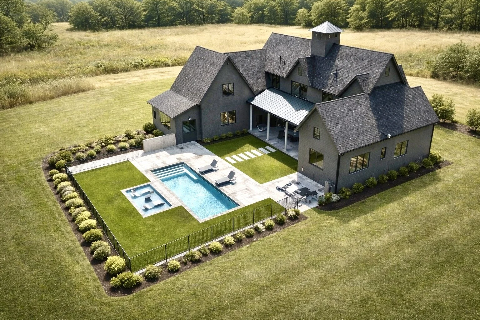 aerial view of a large modern house with a backyard pool, surrounded by a well-maintained lawn and landscaped bushes, set in a spacious outdoor area with trees in the distance.