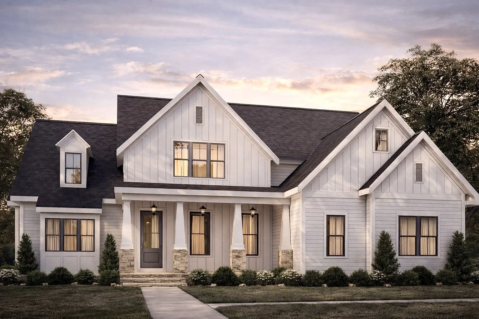 A large white house with a dark roof and stone accents on the front porch, surrounded by trees and grass, at sunset.