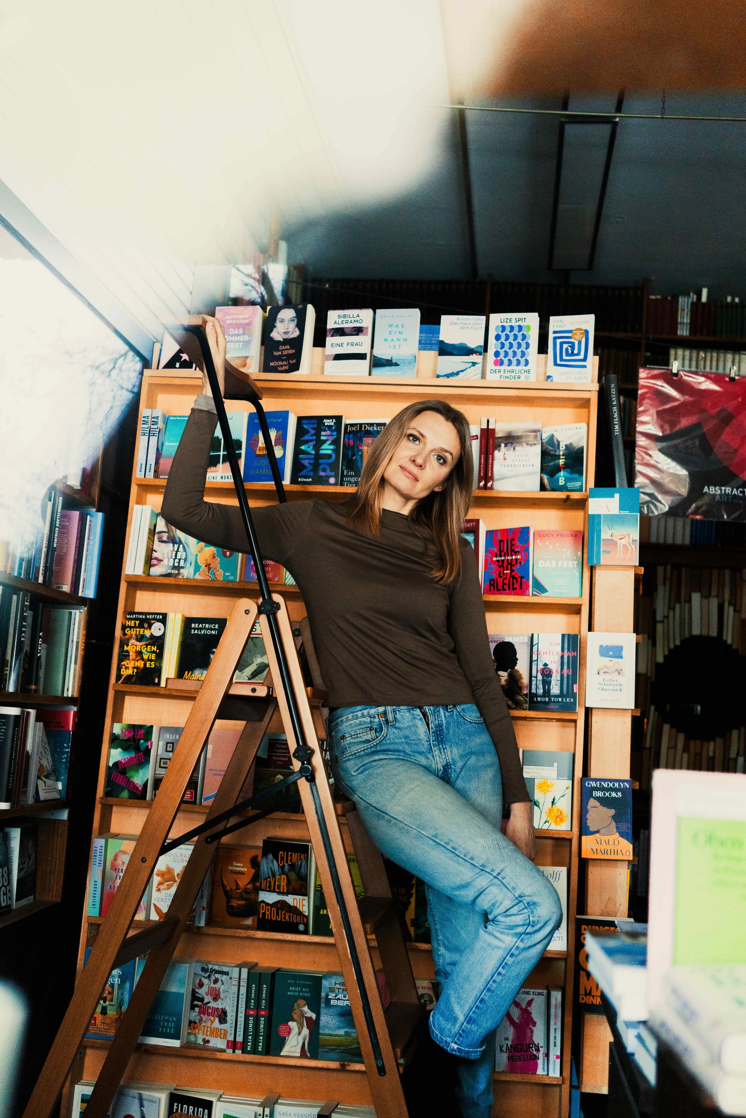 Junge Frau posiert in einer Buchhandlung vor einem Bücherregal, mit einem Leiter.