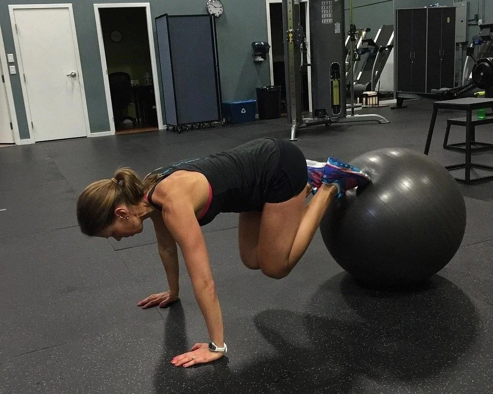A woman doing a hip lift exercise on a fitness ball in a gym.