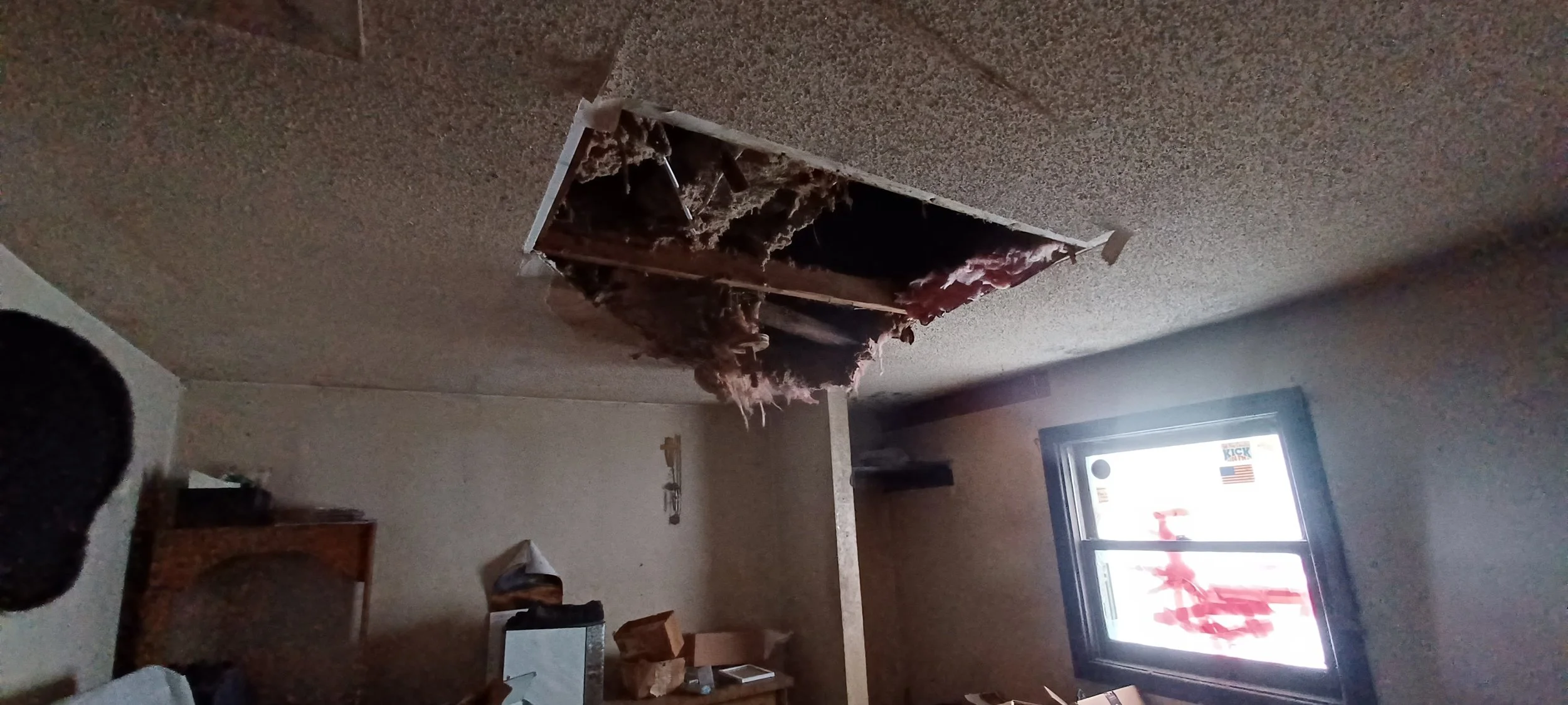 Ceiling with a large hole exposing insulation and wooden beams, with debris hanging down.