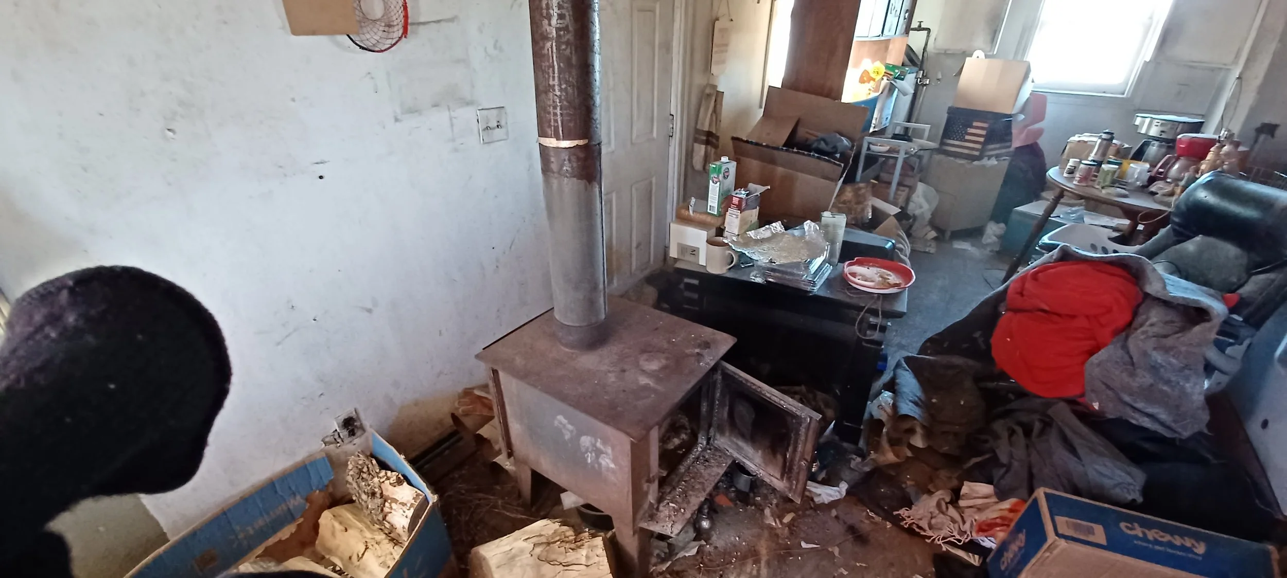 Living room with clutter, messy furniture, and a wood stove.