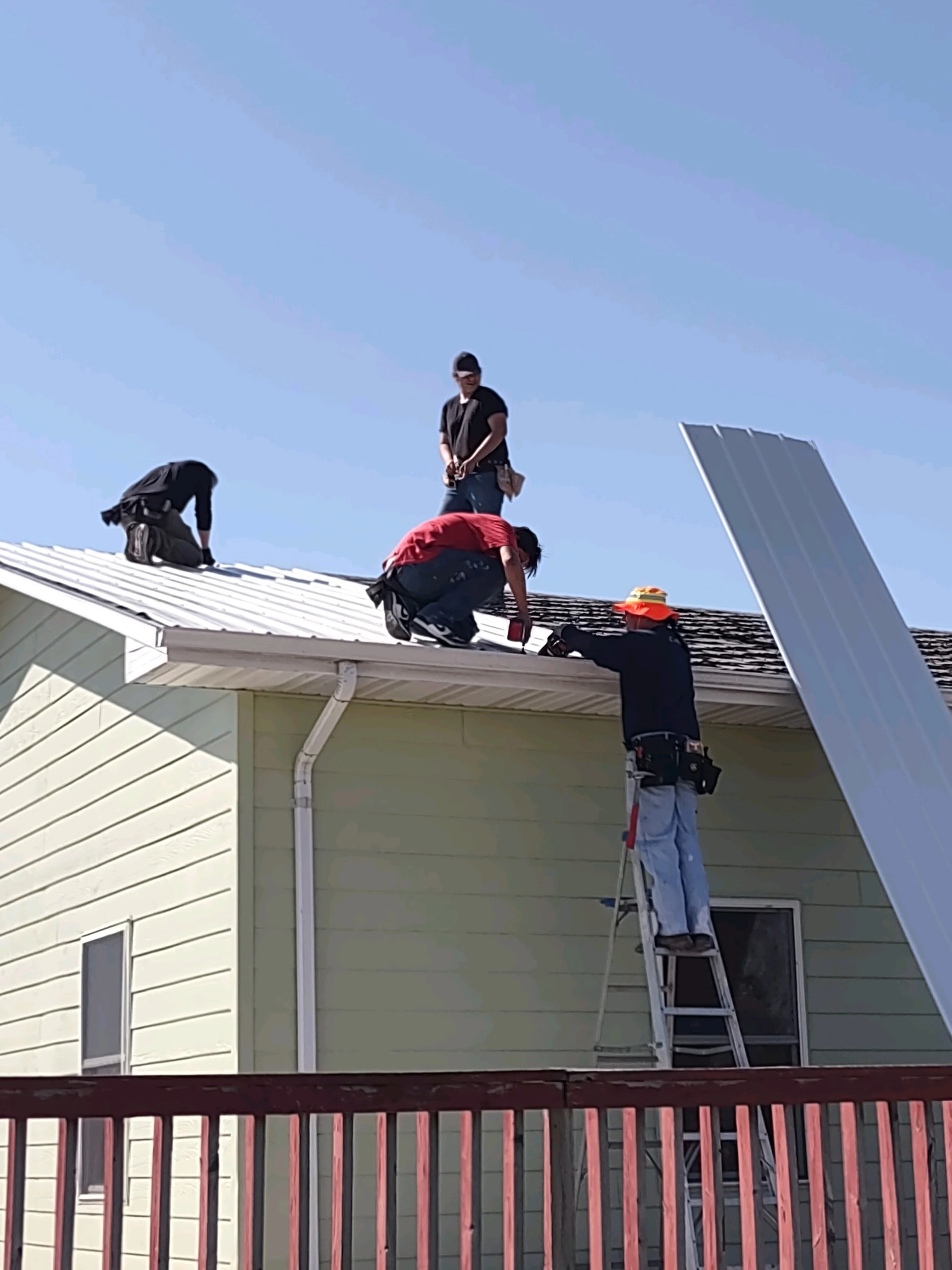 Four workers installing or repairing solar panels on the roof of a yellow house under a clear blue sky.