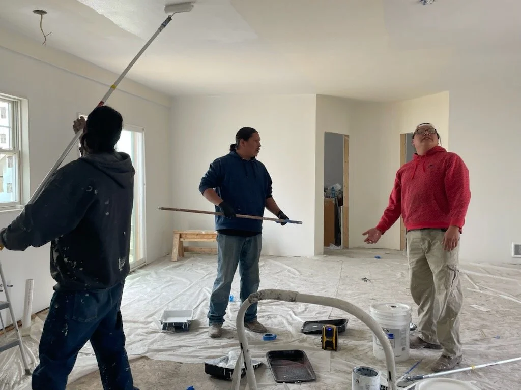 Three people working on a home renovation, painting and preparing the interior space with tools, paint, and materials.