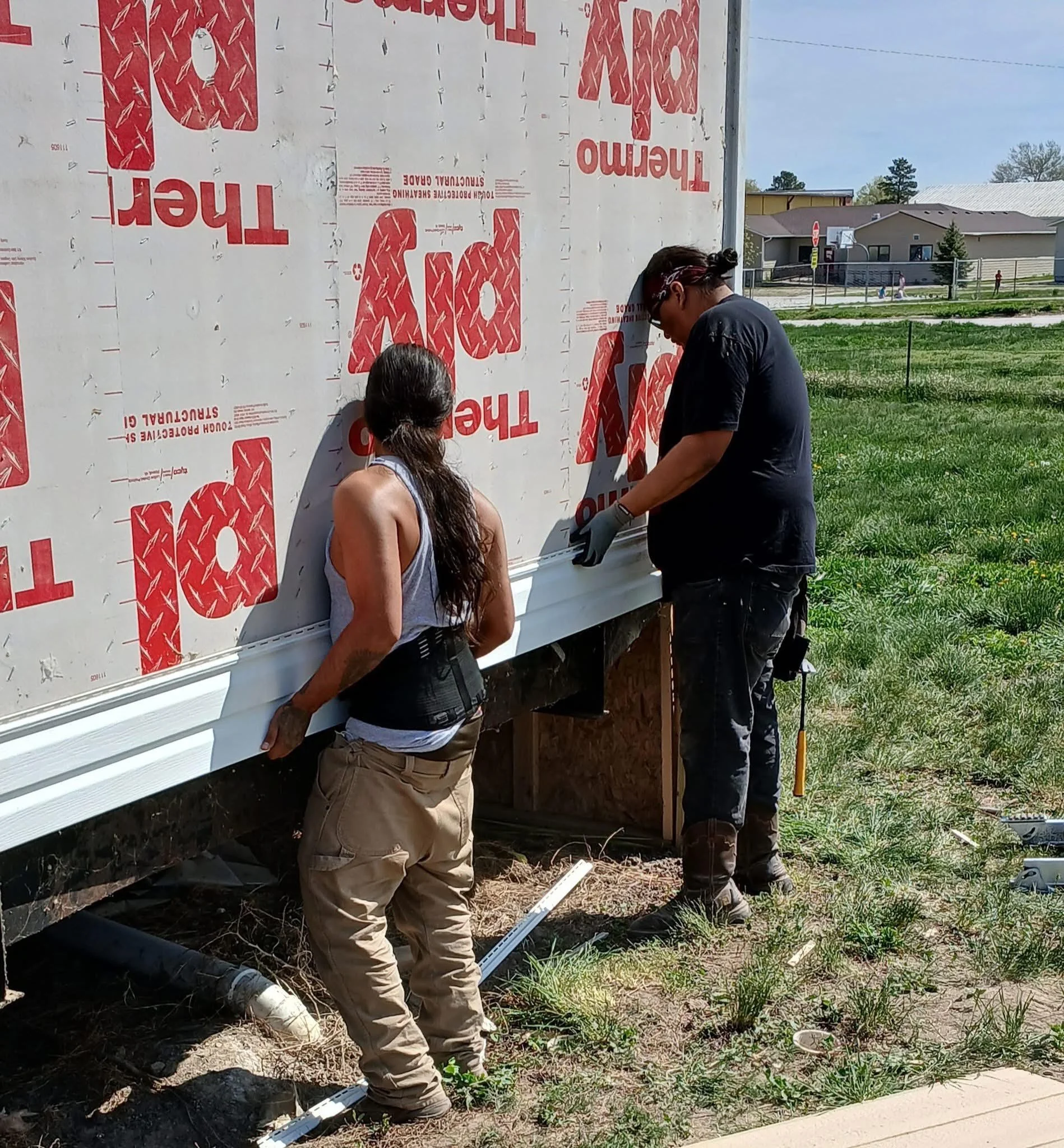 Two workers installing siding on a house in a grassy area.
