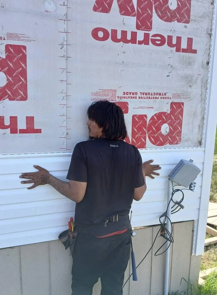 Person installing or inspecting siding on a building with insulation panels and a mounted electrical box.