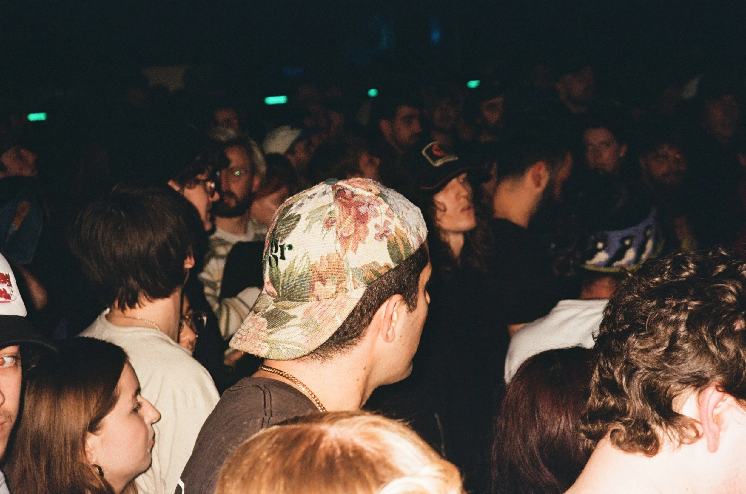 Crowd of people at a concert or event, some with hats, facing a stage or focal point not visible in the image.