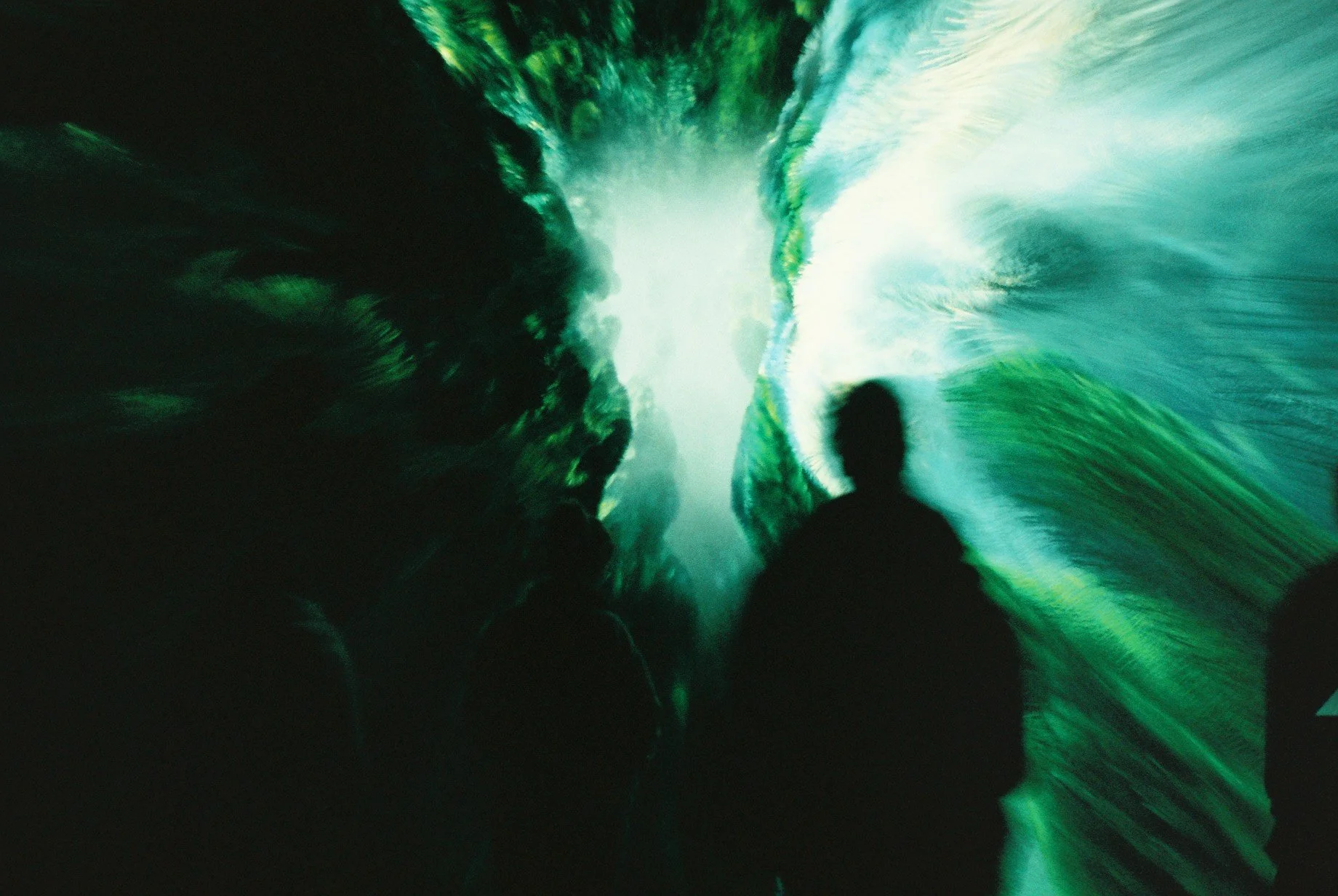 People observing an immersive digital art installation with green and blue swirling visuals.