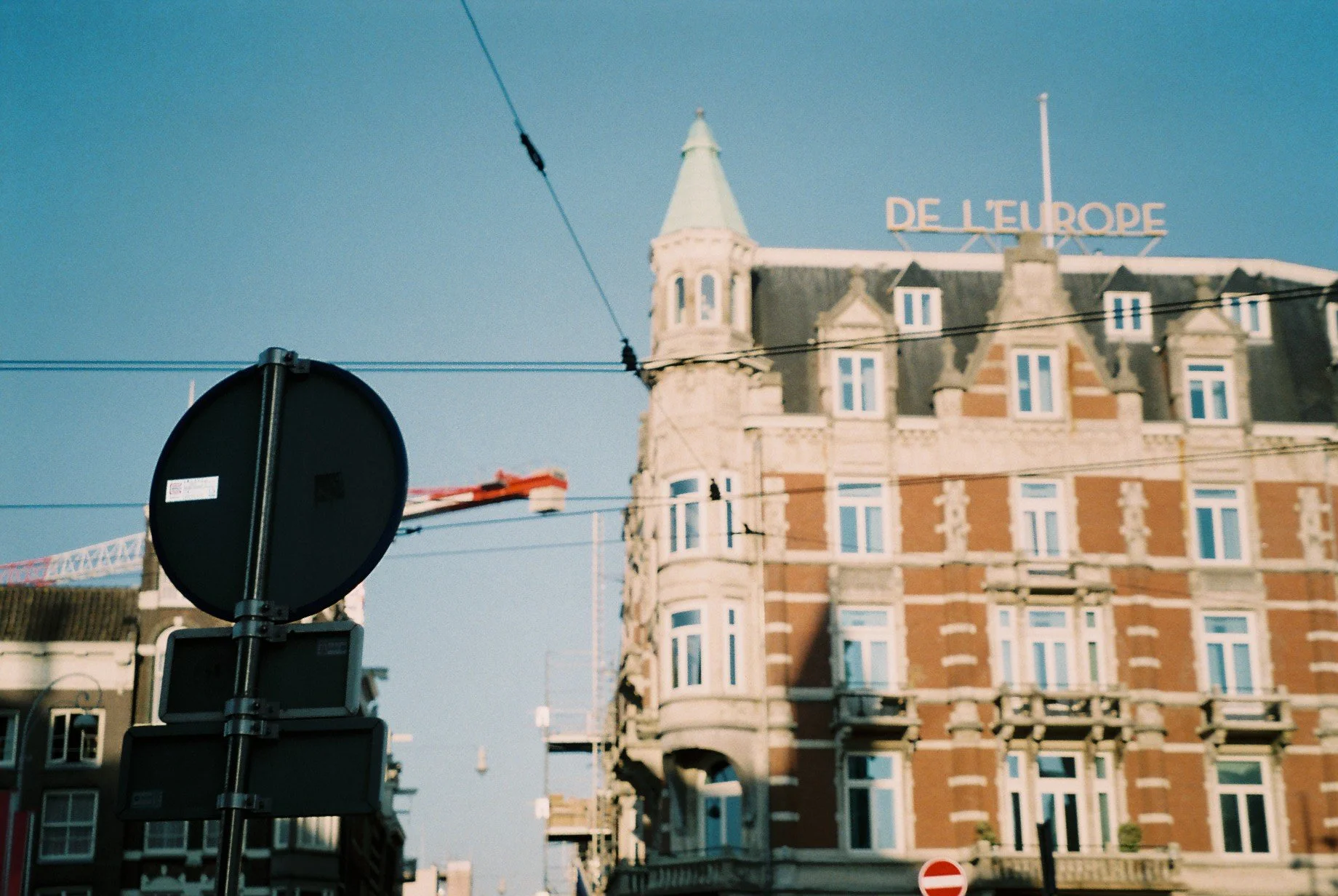 Photo of a European-style building with a turret, window balconies, and a rooftop sign that reads 'DE L'EUROPE'. Overhead wires and road signs are visible in the foreground.