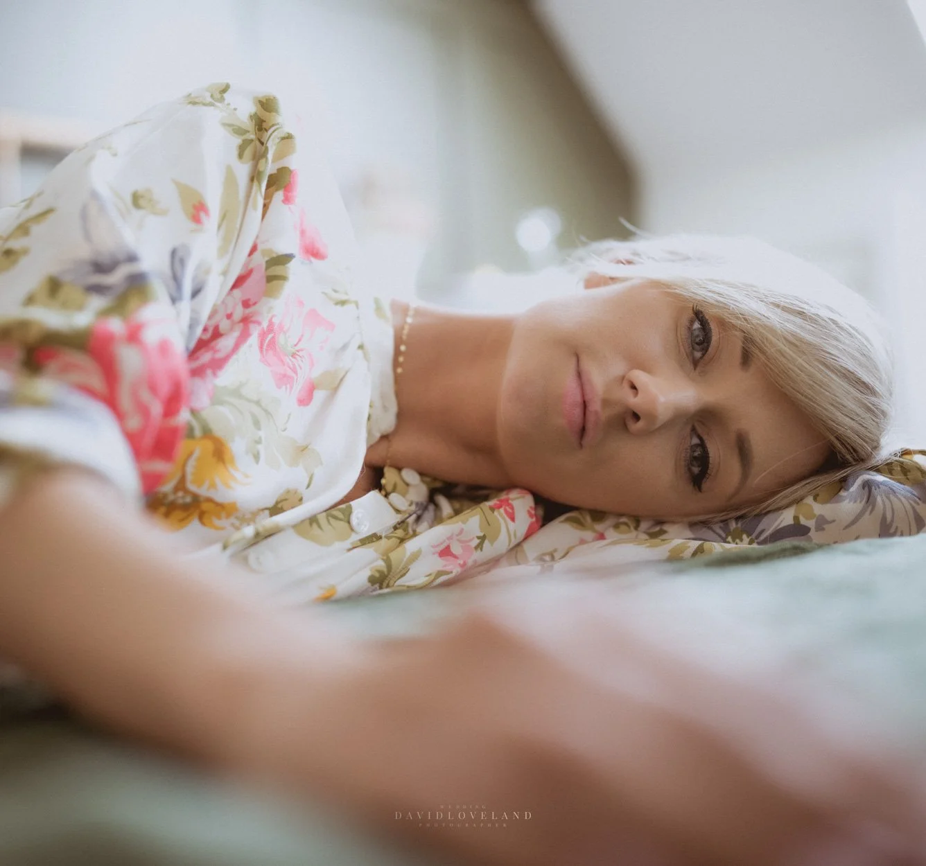 Beautiful blonde model in summer, floral H&M dress. Blue eyes, lying on bed. David Loveland fashion photography and Styling.  