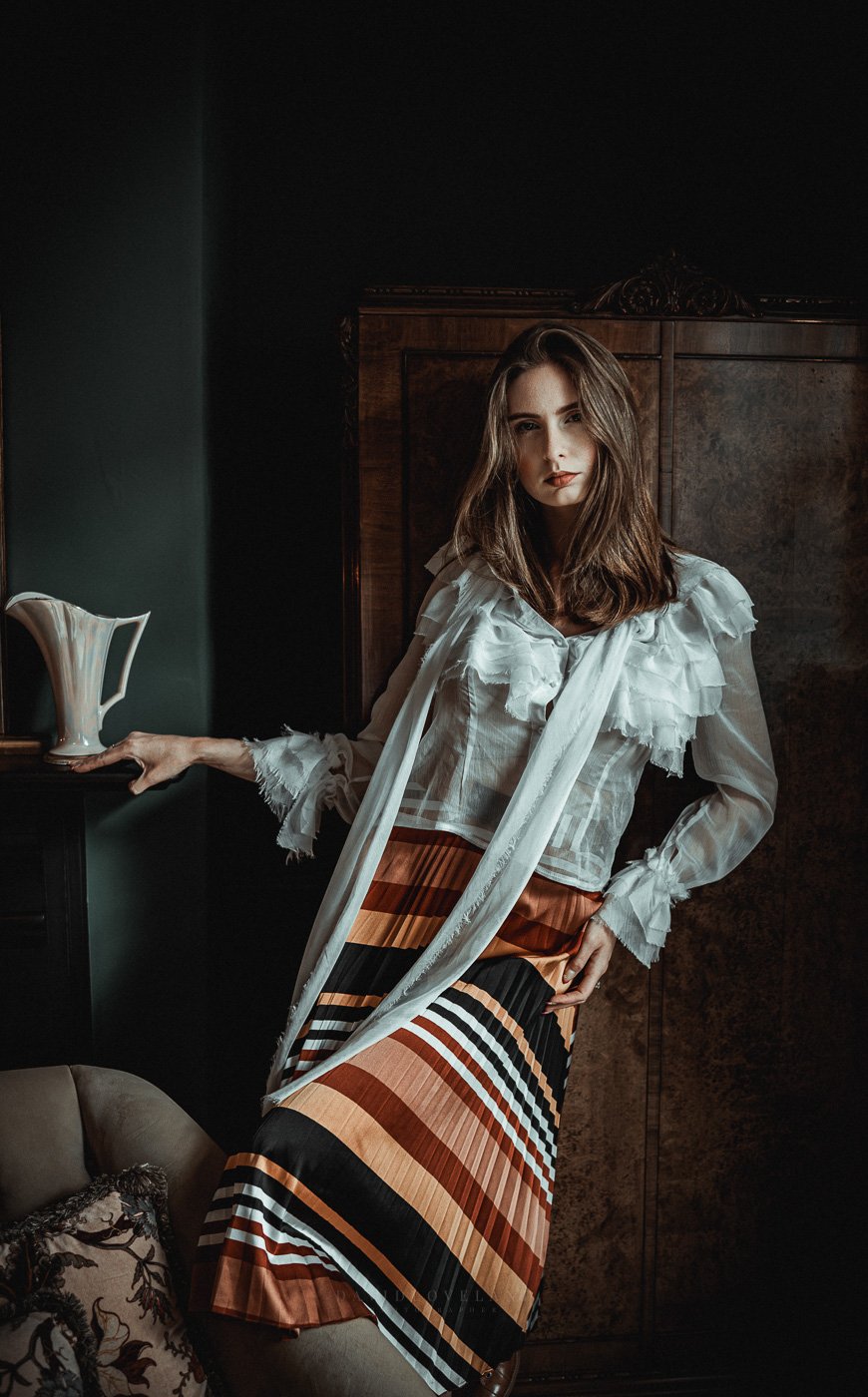 Tall beautiful fashion model wearing ruffled white blouse and pleated satin orange and yellow skirt in opulent Georgian house, David Loveland Fashion Photography