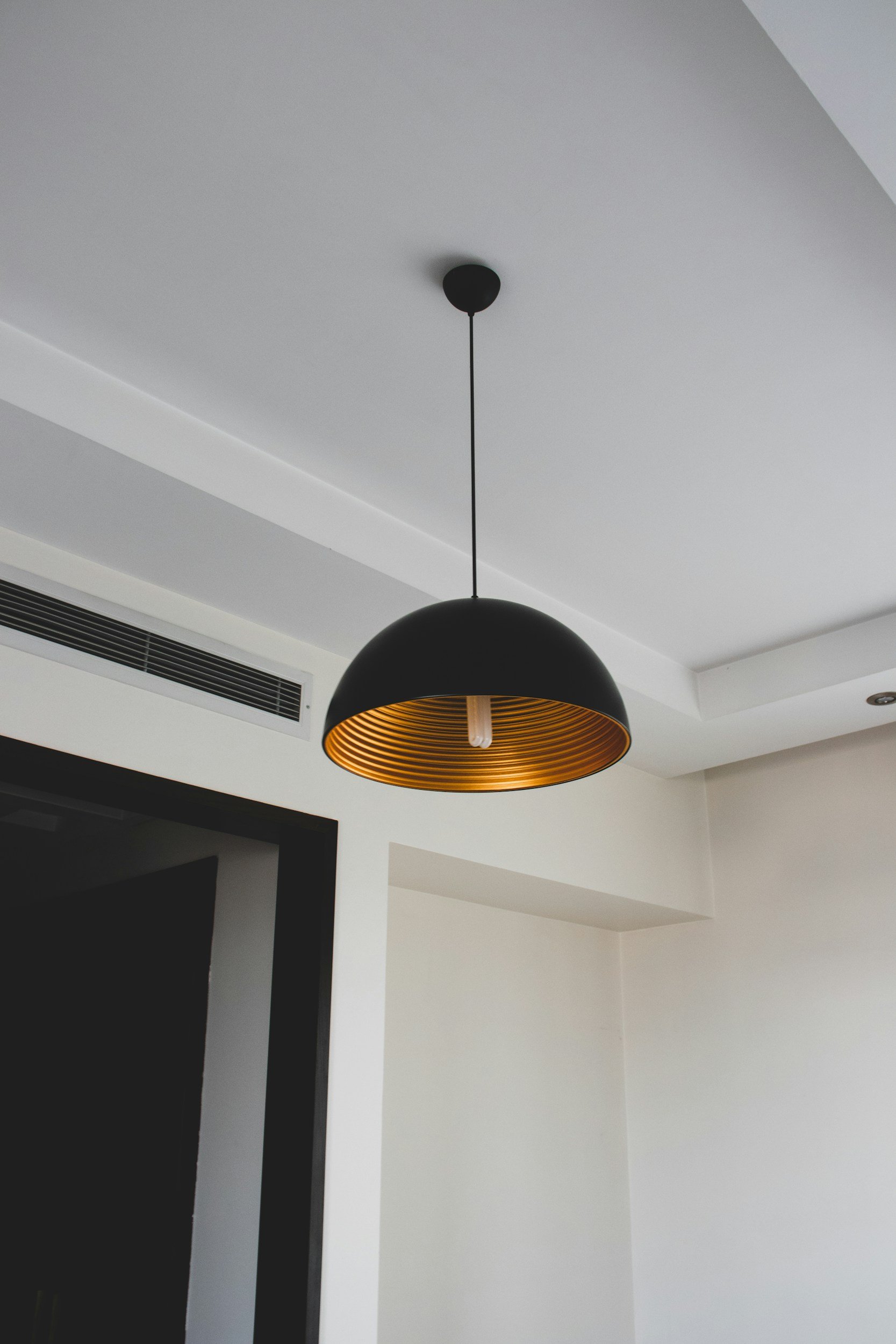 Black pendant light with a gold interior hanging from a white ceiling in a modern interior space.