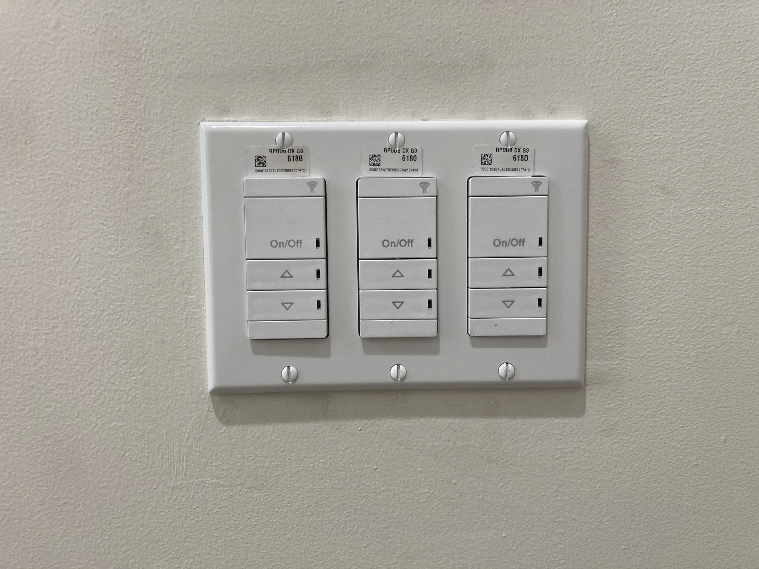 White three-gang light switch plate with three switches, each with up and down arrows, mounted on a beige wall.