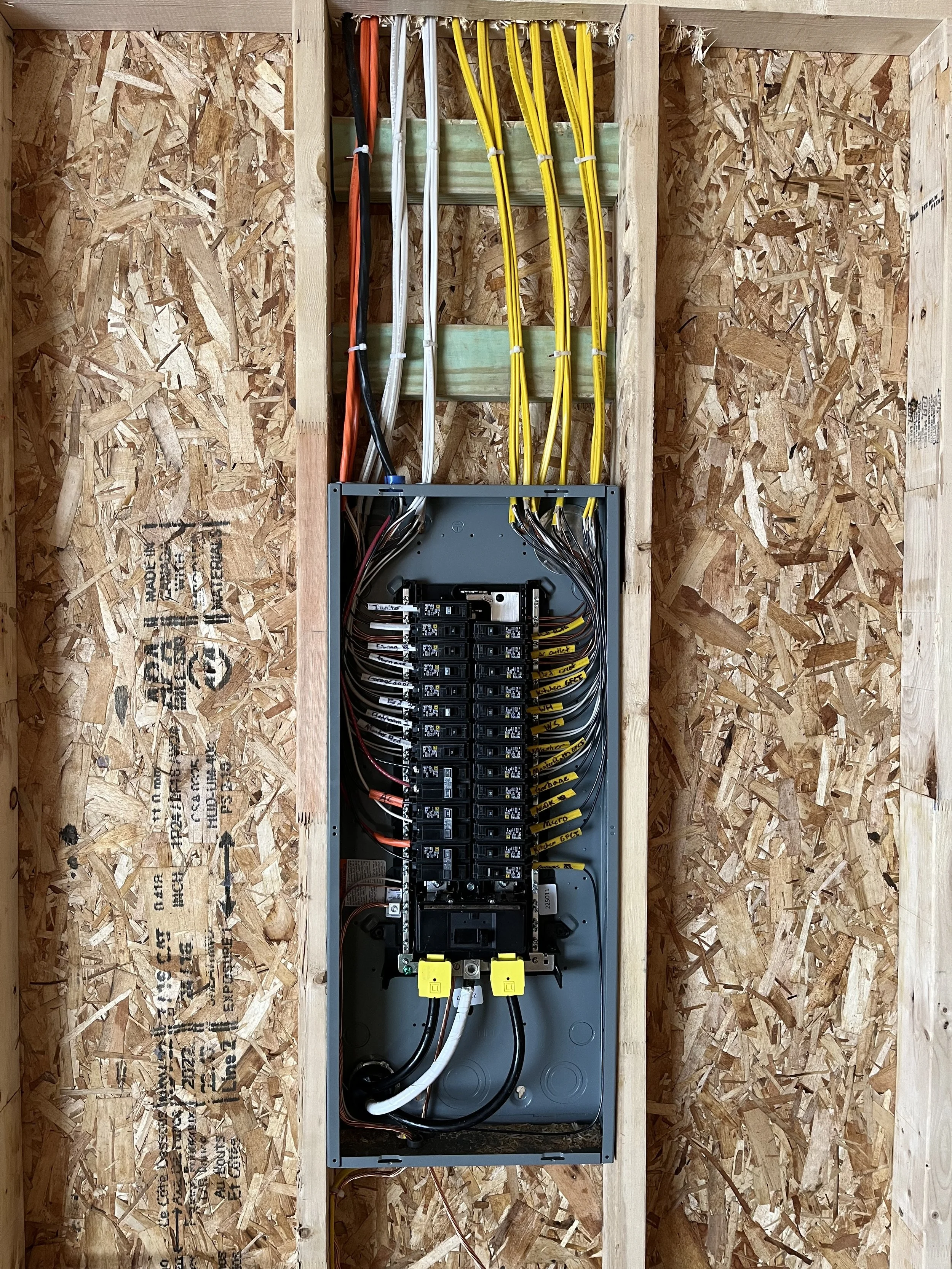 Open electrical breaker box with organized wires inside a wooden wall.