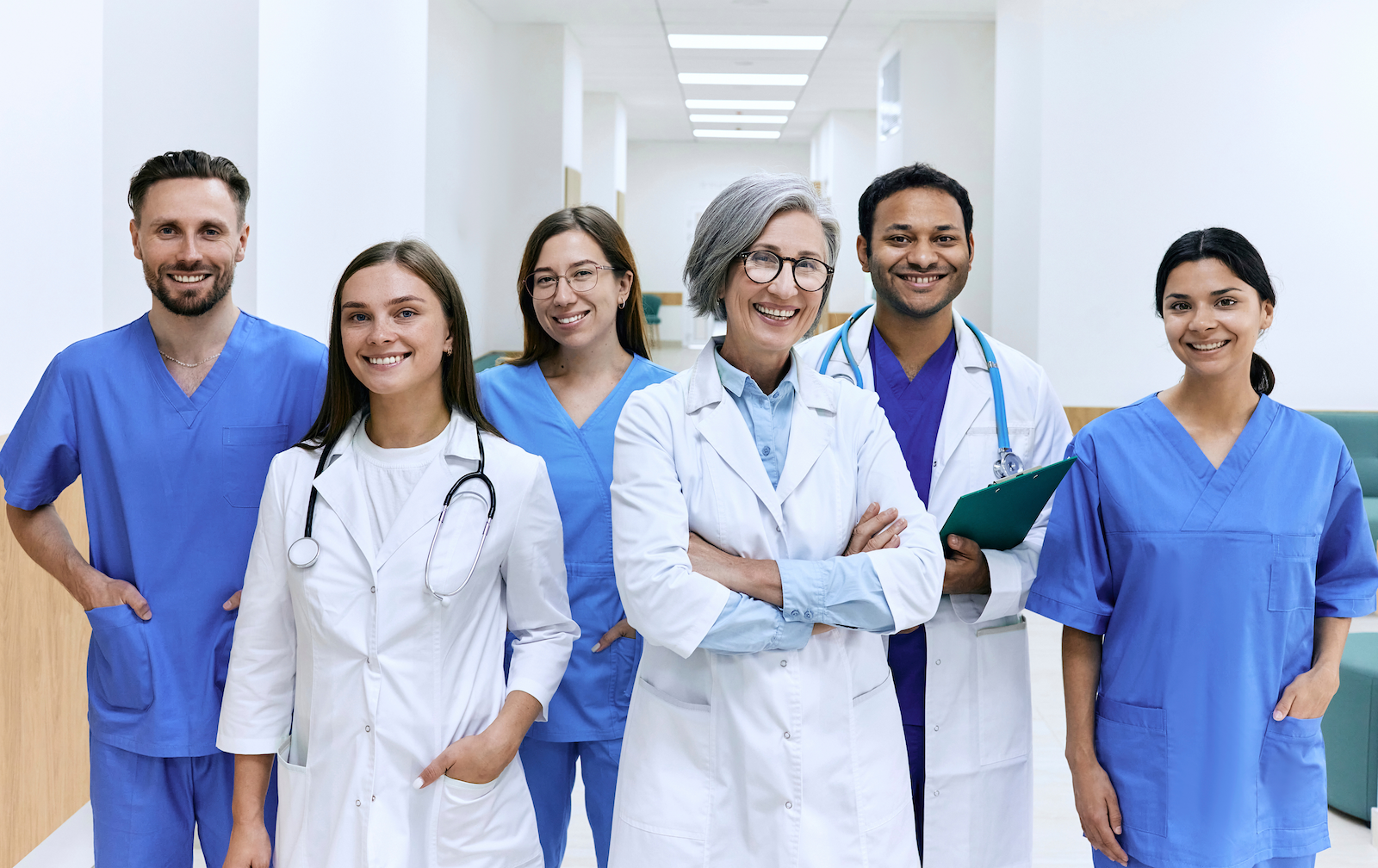 Group of diverse healthcare professionals and doctors standing in hospital corridor, smiling.