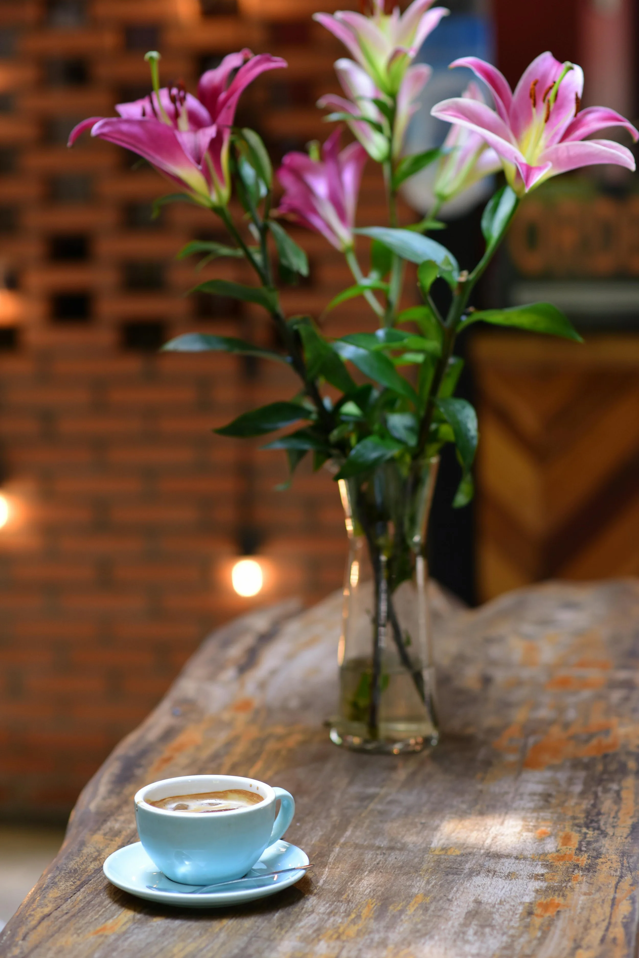 A vase of beautiful flowers and blue coffee cup with saucer, a top a wooden table