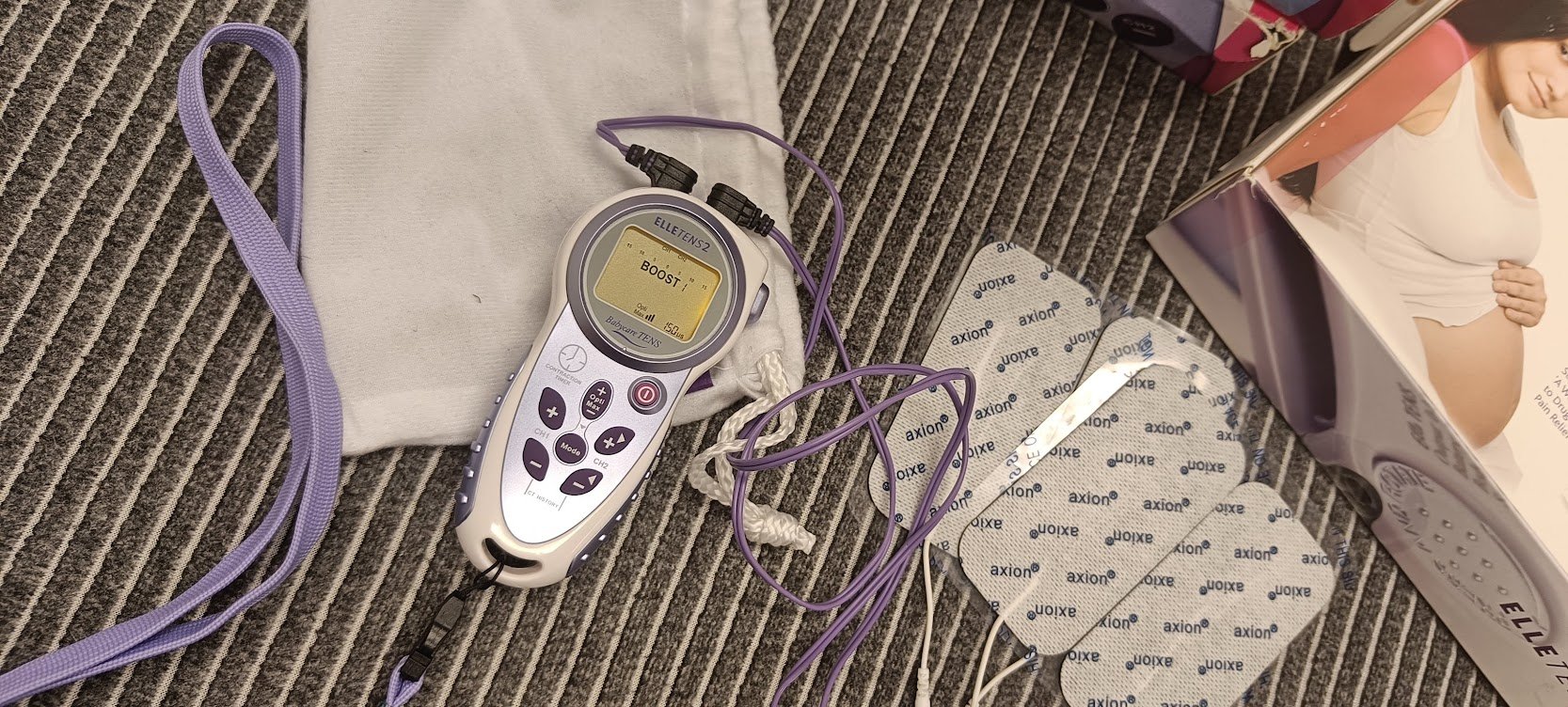 Tens-laite harmaan pyyhkeen päällä laatikon sekä tens-elektrodien vieressä. Tens Turku, tens-laitteen vuokraus.