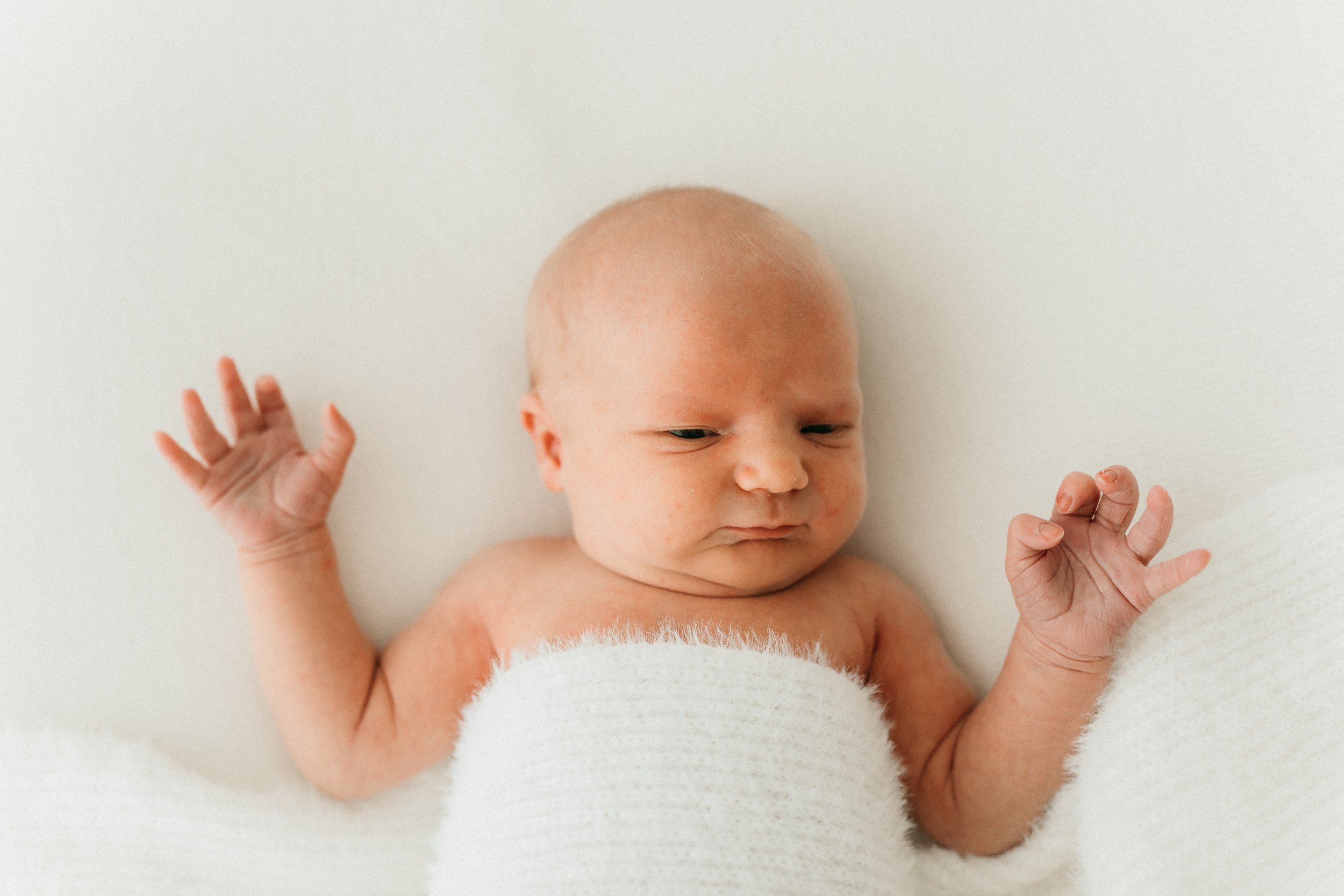 Kuvassa vauvan ylävartalo. Makaavalla vauvalla on kädet ylhäällä. Valkoinen kangas peittää vauvan rintäkehän.