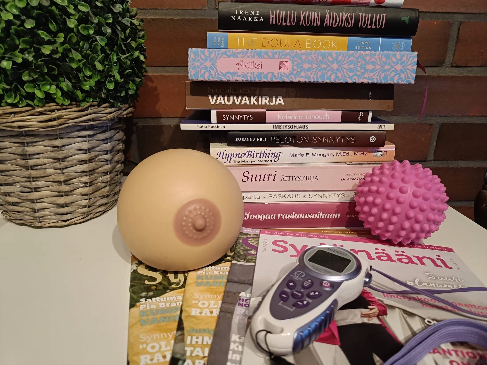 Kuvassa on pöydällä kasa raskaus- ja äitiys-aiheisia kirjoja, hierontapallo, tekorinta sekä tens-laite.