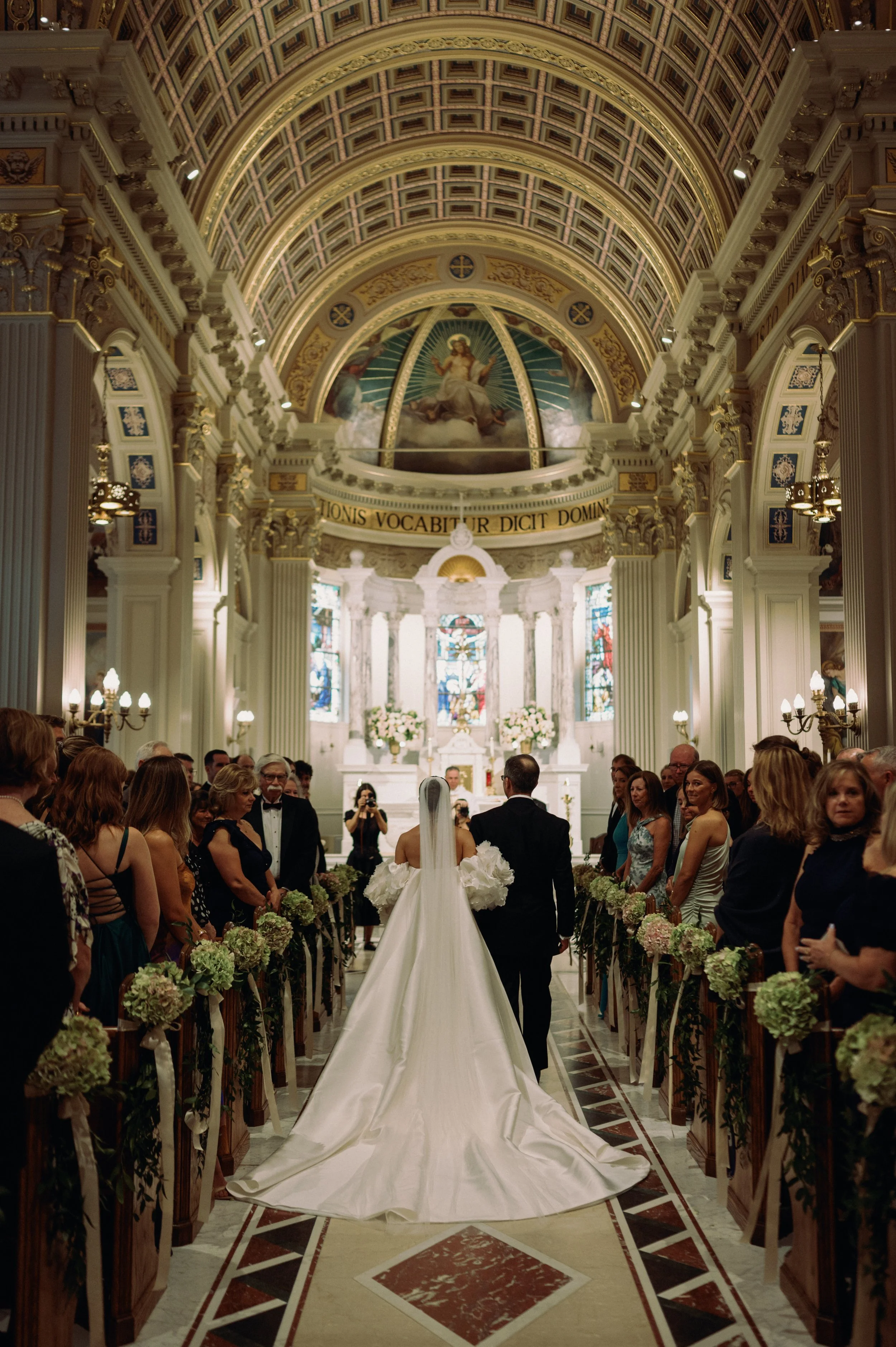A bride and groom walk down the aisle in a church during a wedding ceremony, with guests on both sides watching them.