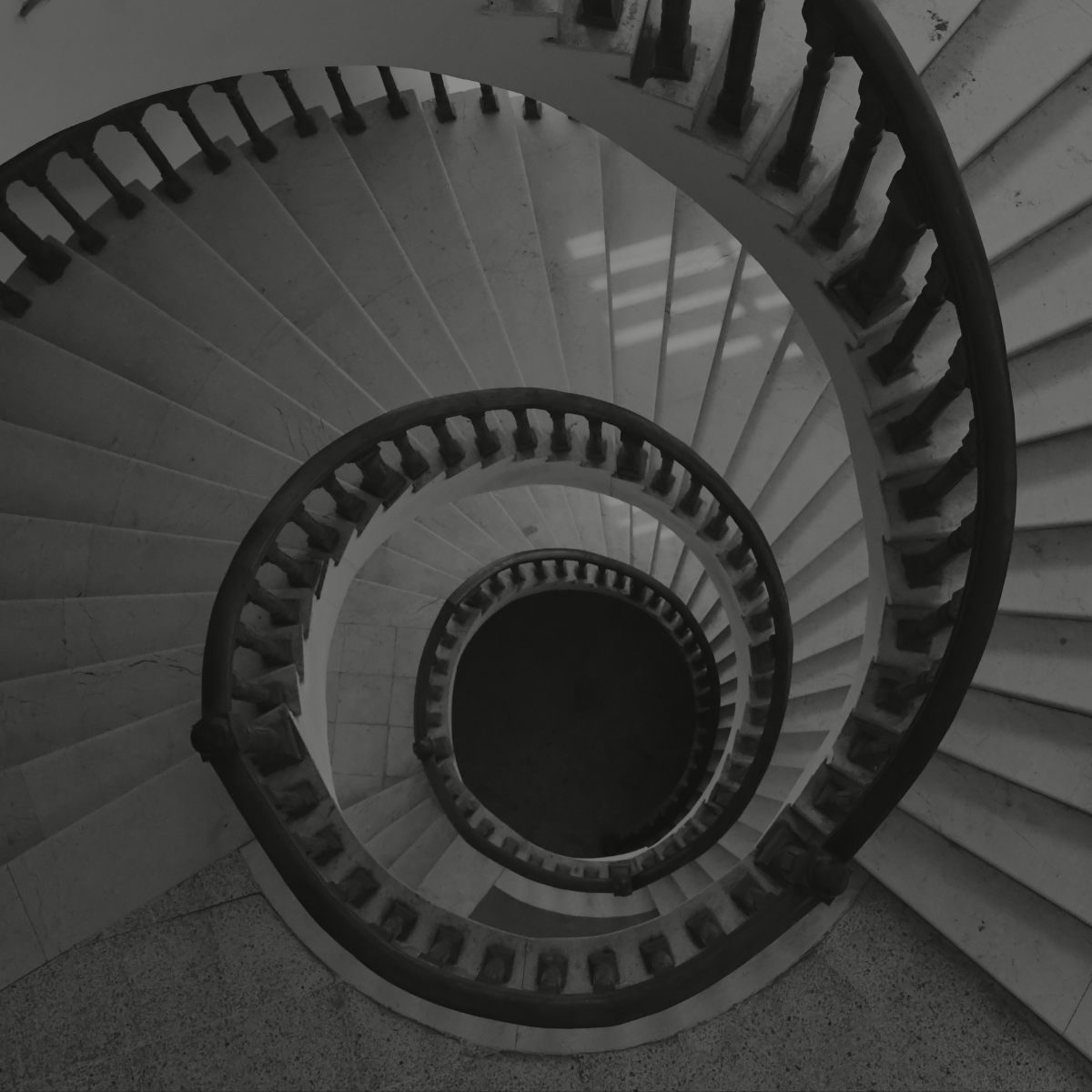 Top-down view of a spiral staircase with marble steps and wooden railings, creating a vortex pattern.