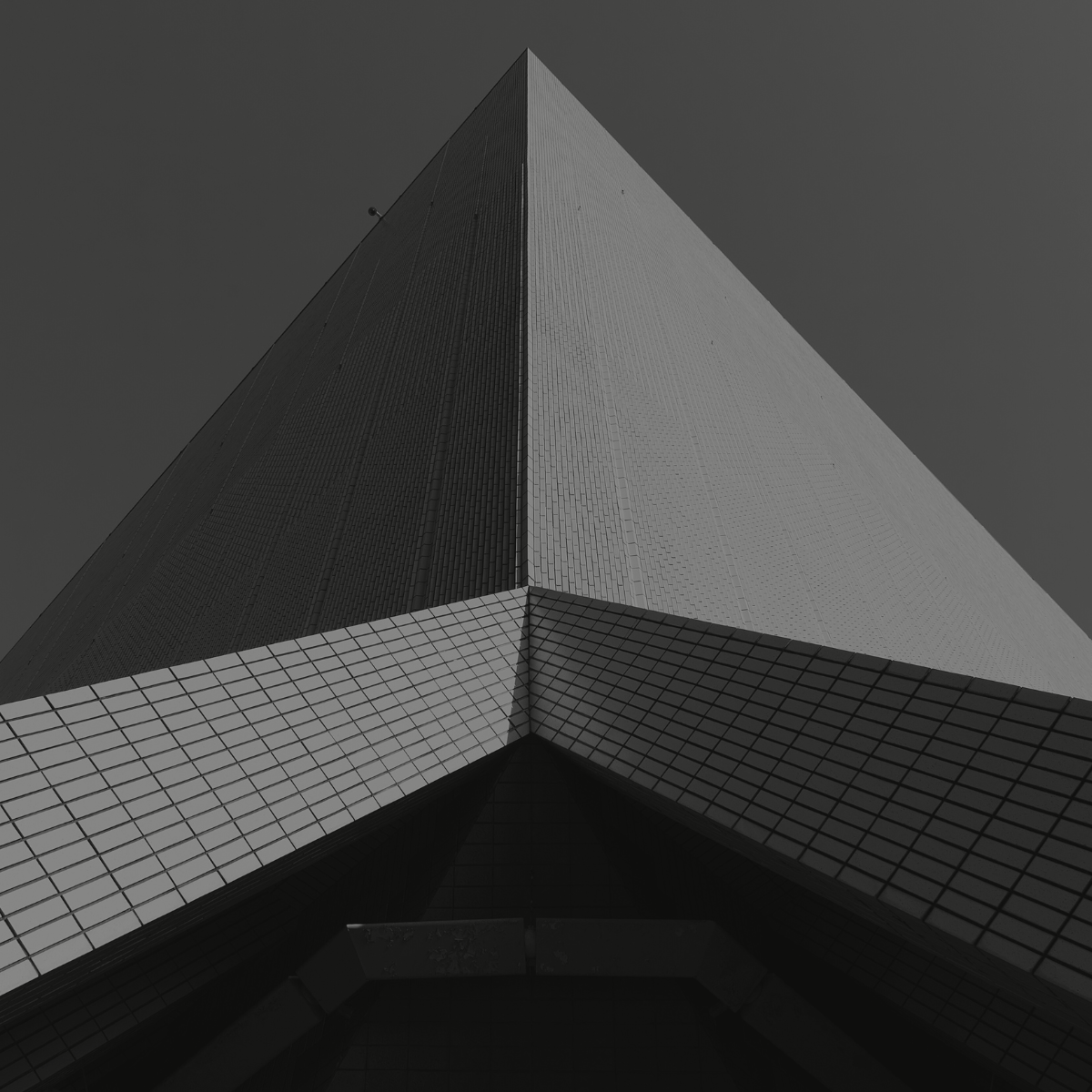 Black and white photo of a tall, modern building with a sharp, triangular roof shape, taken from a low angle looking up.
