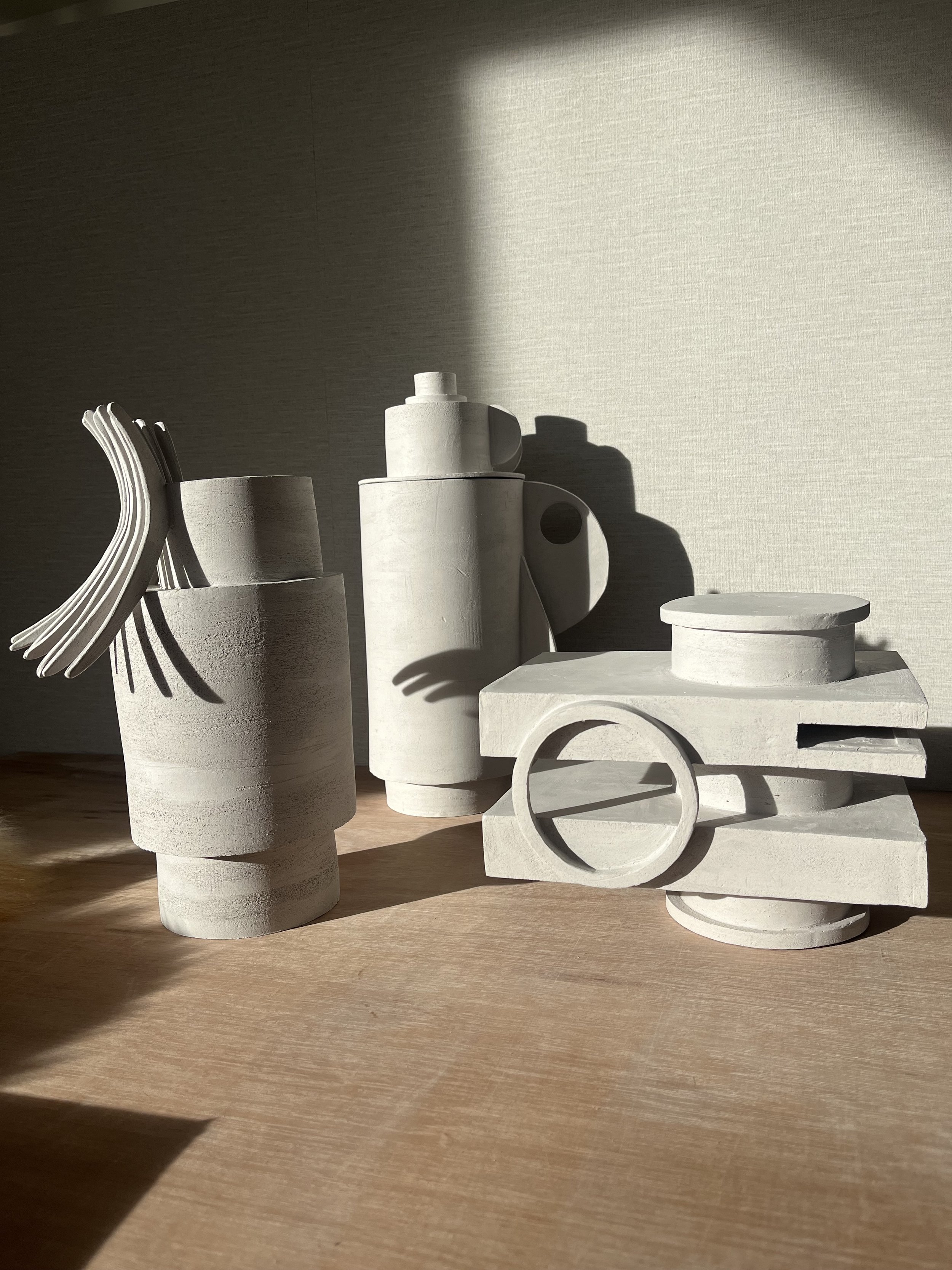 Abstract white sculptural objects with geometric shapes arranged on a wooden surface, illuminated by sunlight and casting shadows.