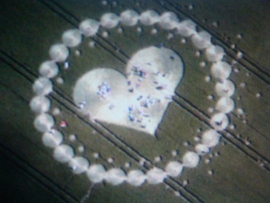 Heart shape outlined with white pebbles on a wooden surface, with a smaller heart cutout filled with confetti.