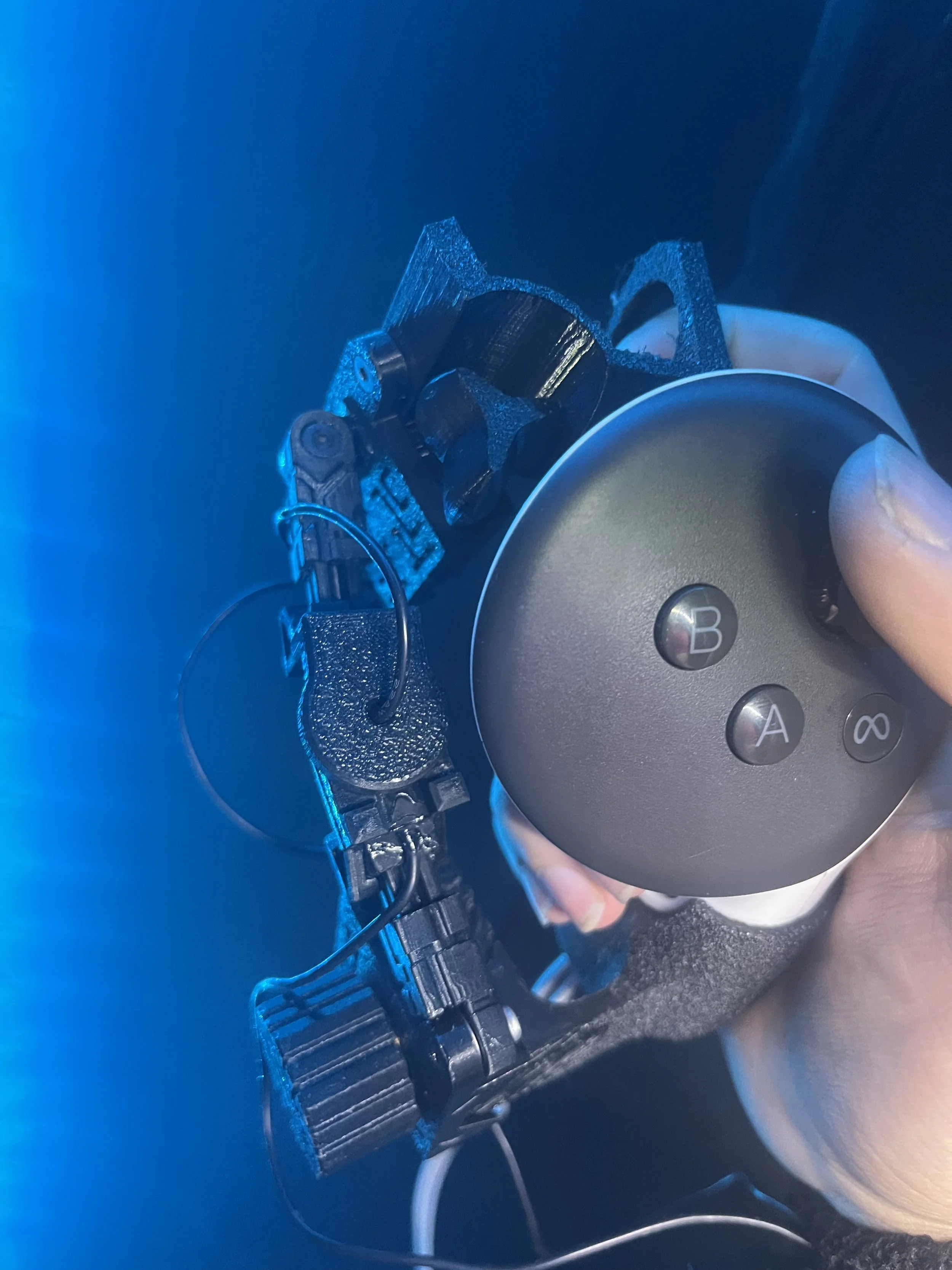Close-up of a person holding a VR controller, with a robotic or mechanical structure in the background, illuminated by blue light.