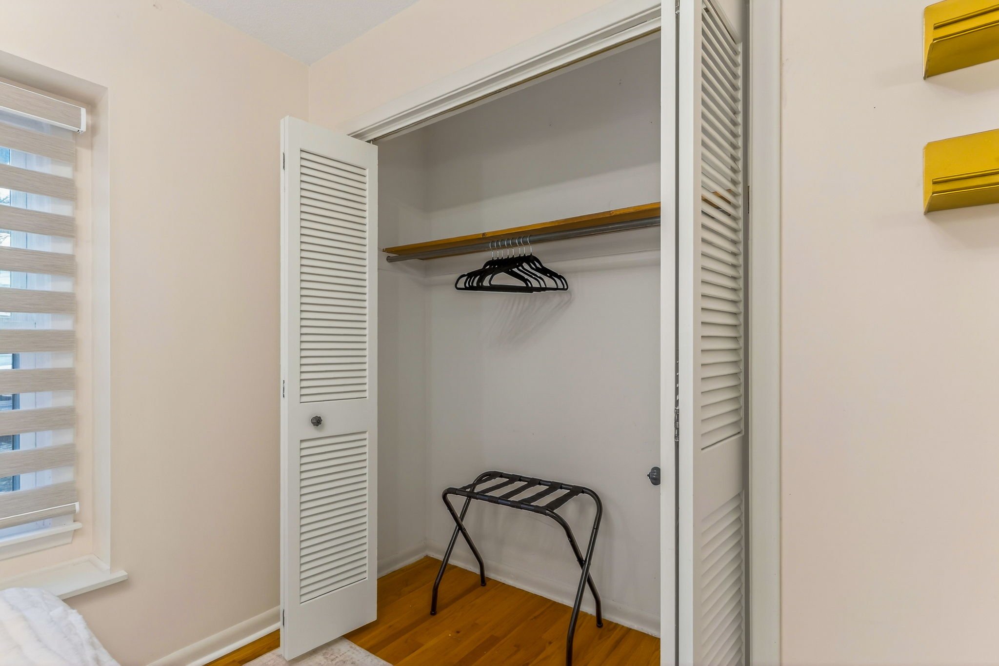 Empty closet with open sliding doors, a wooden shelf, black hangers, and a foldable luggage rack.
