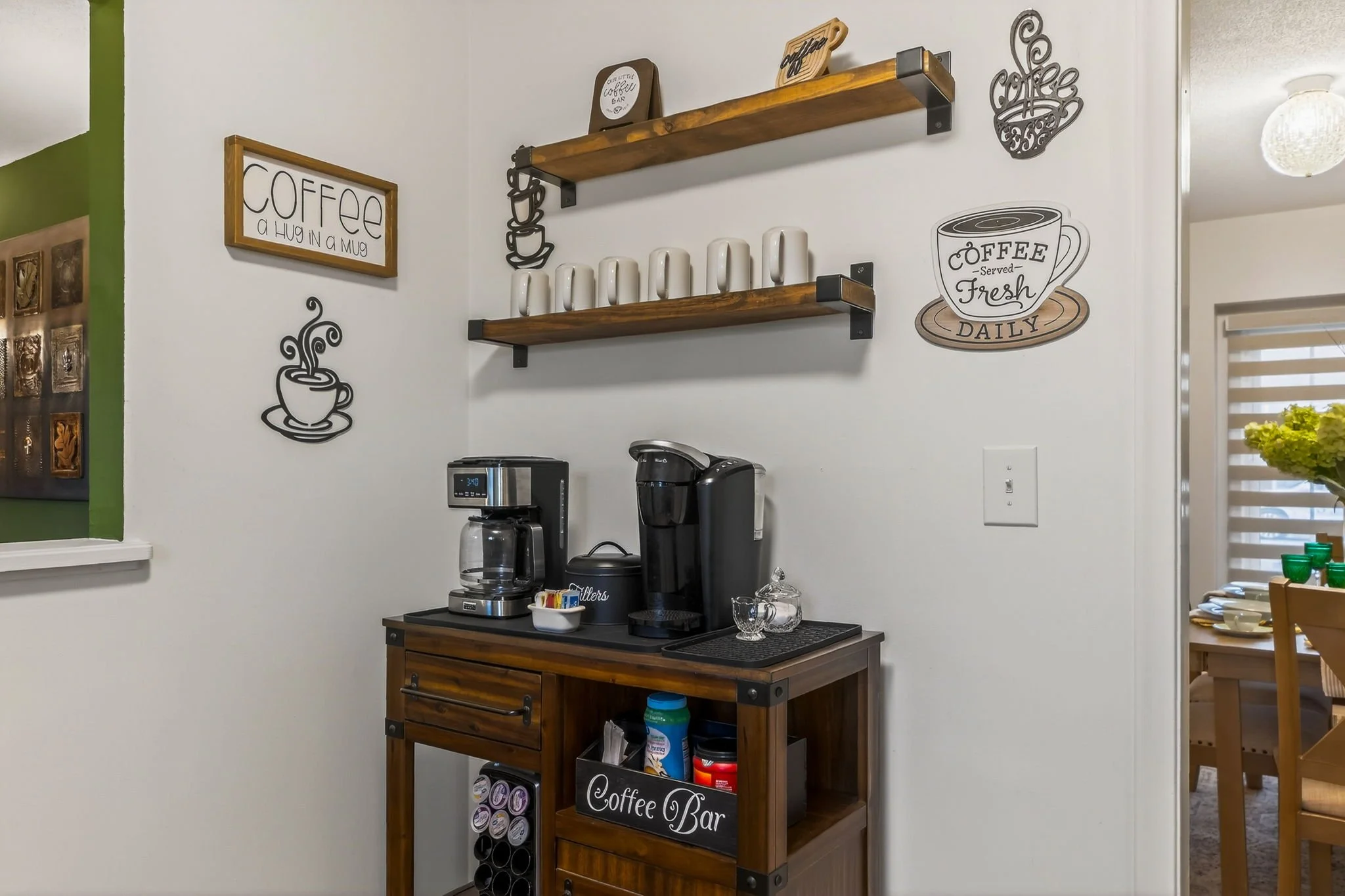 Coffee station with coffee maker, mugs, and decorative wall signs in a home.