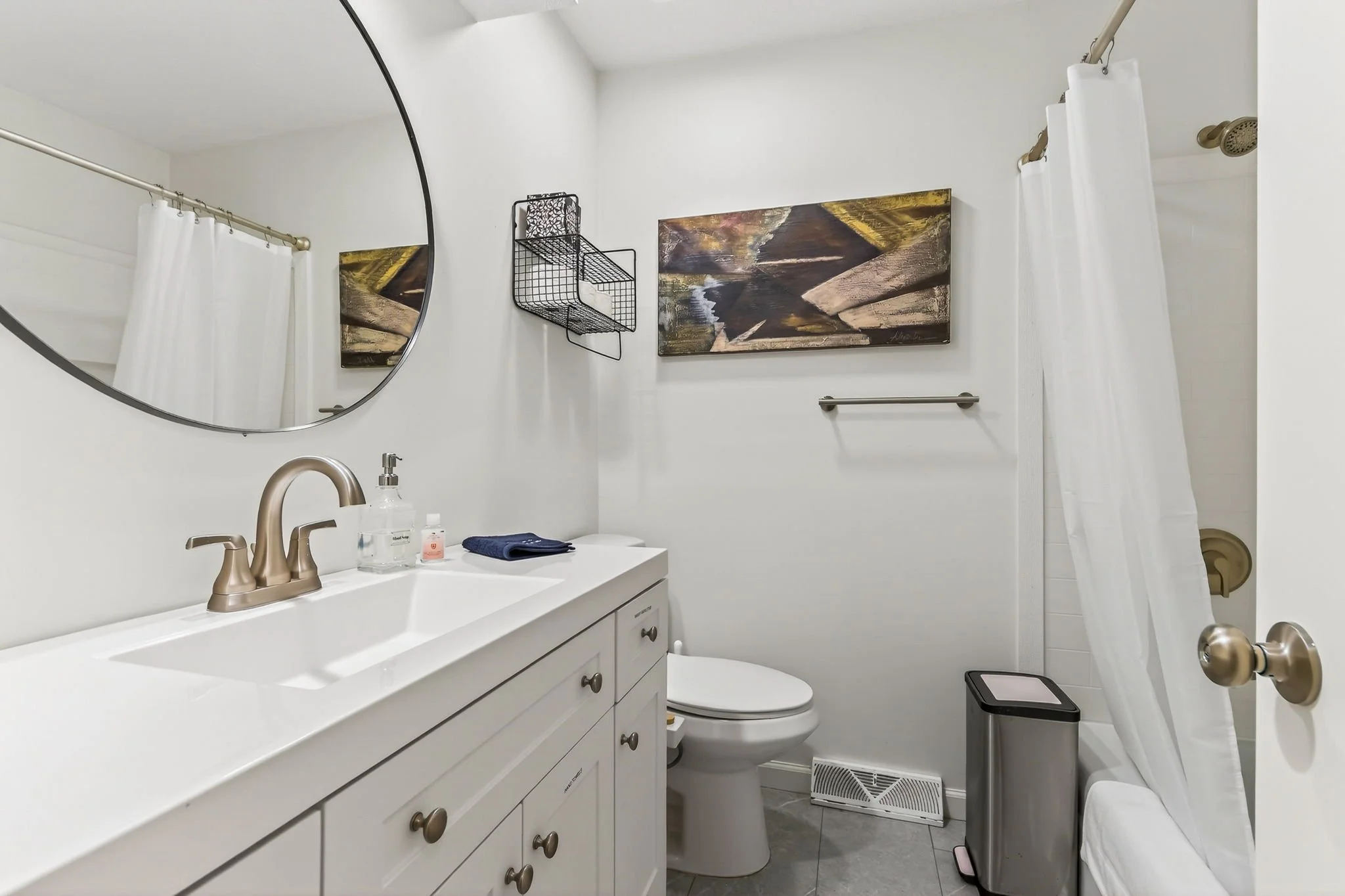 Small bathroom with white vanity, oval mirror, and white shower curtain.