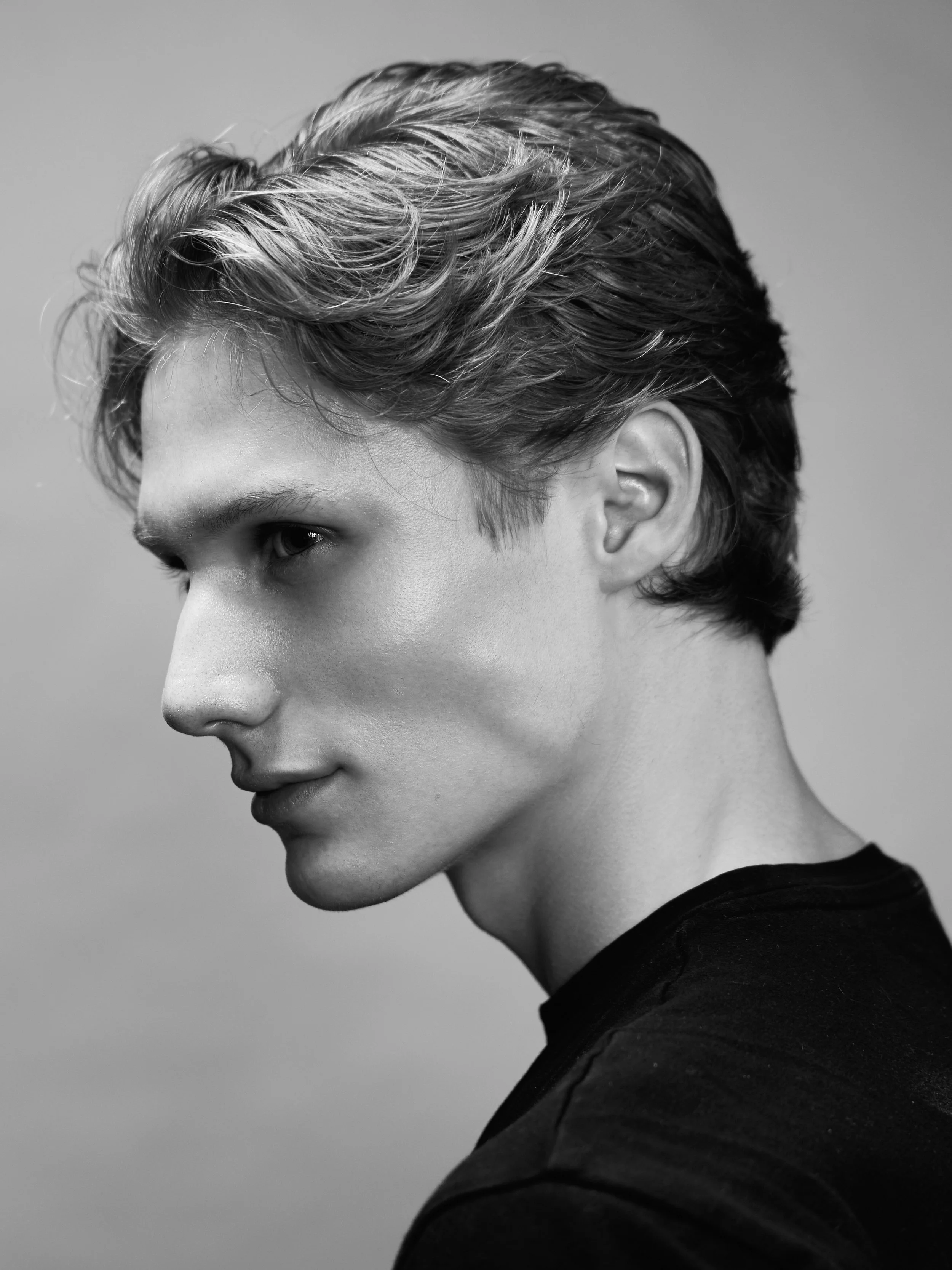 A black and white profile of a young person with short, wavy hair, wearing a dark shirt, against a plain background.