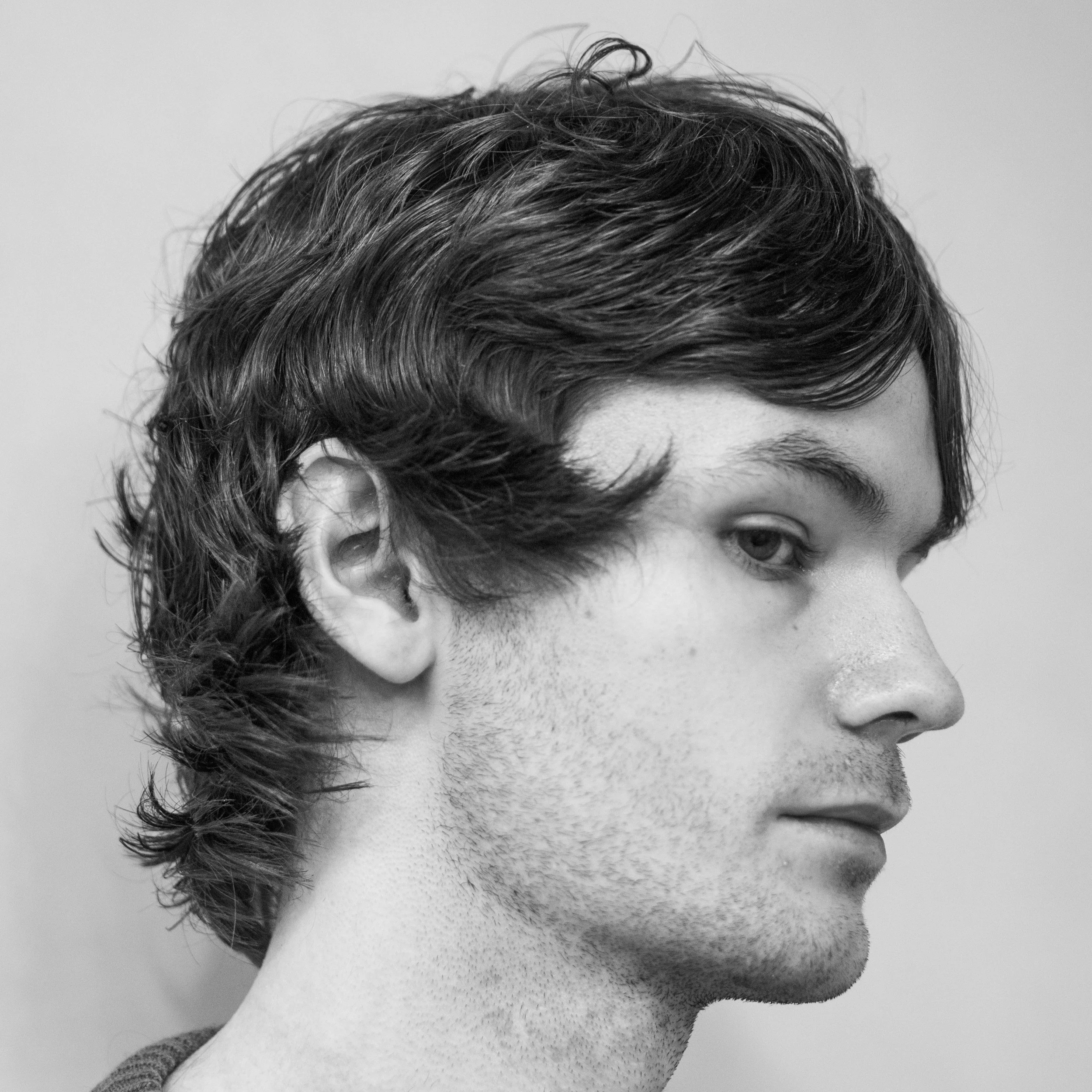 Close-up black and white photo of a young person's face, showing their eye, partial lips, and short wavy hair.