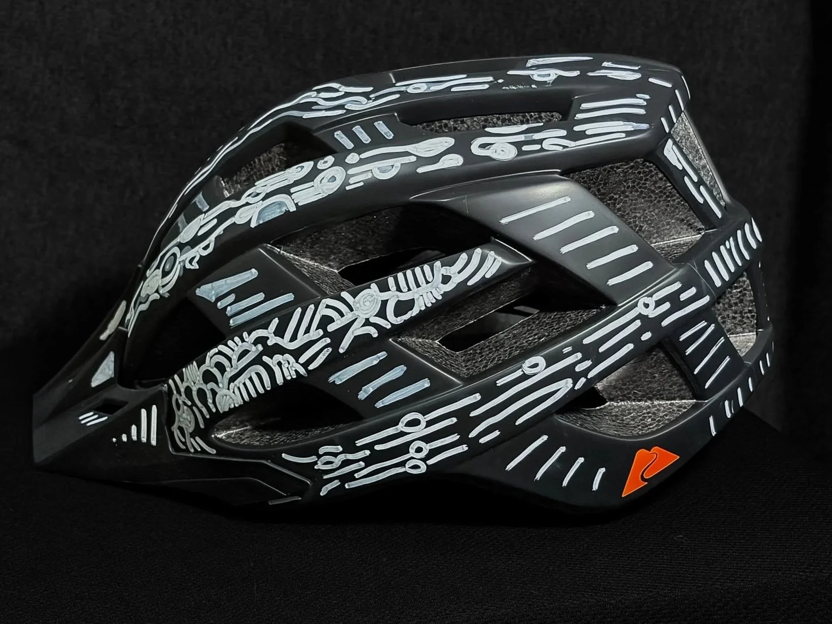 Black bicycle helmet with white abstract line and symbol designs, placed on a black background.