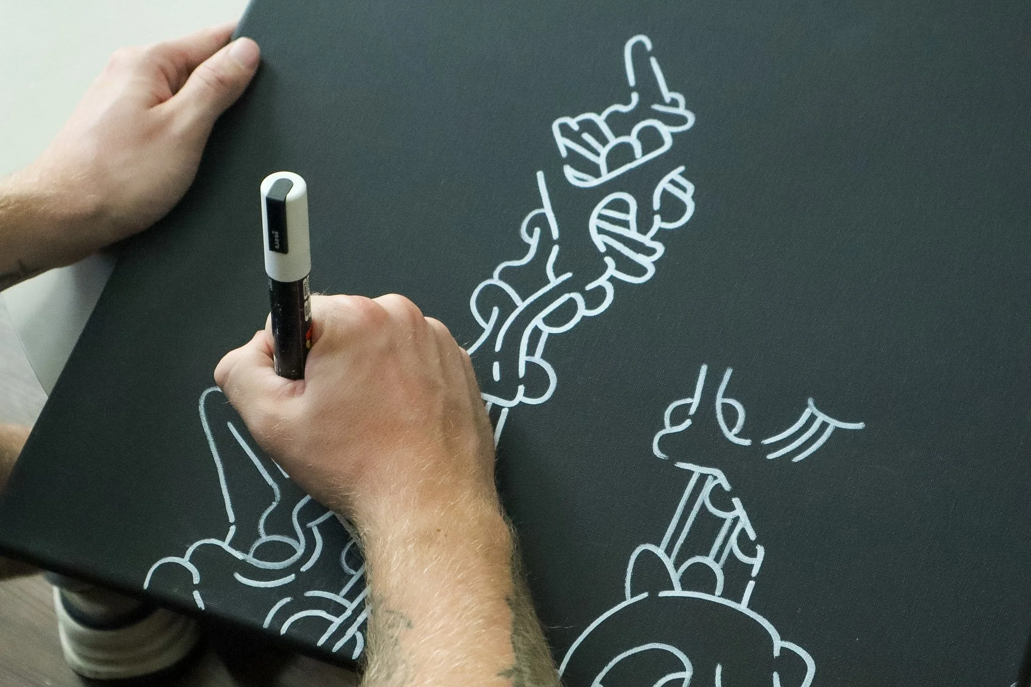 A person drawing a white chalk outline of a skeleton on a dark chalkboard or black surface.