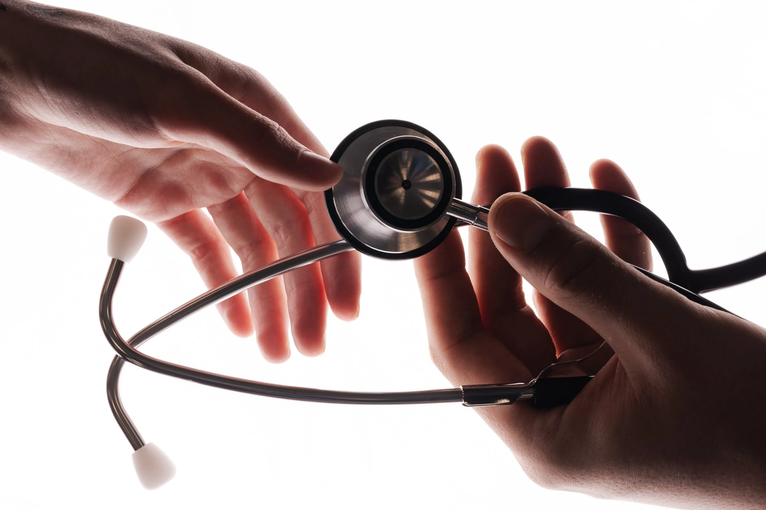 Zwei Hände halten ein Stethoskop vor hellem Hintergrund.
