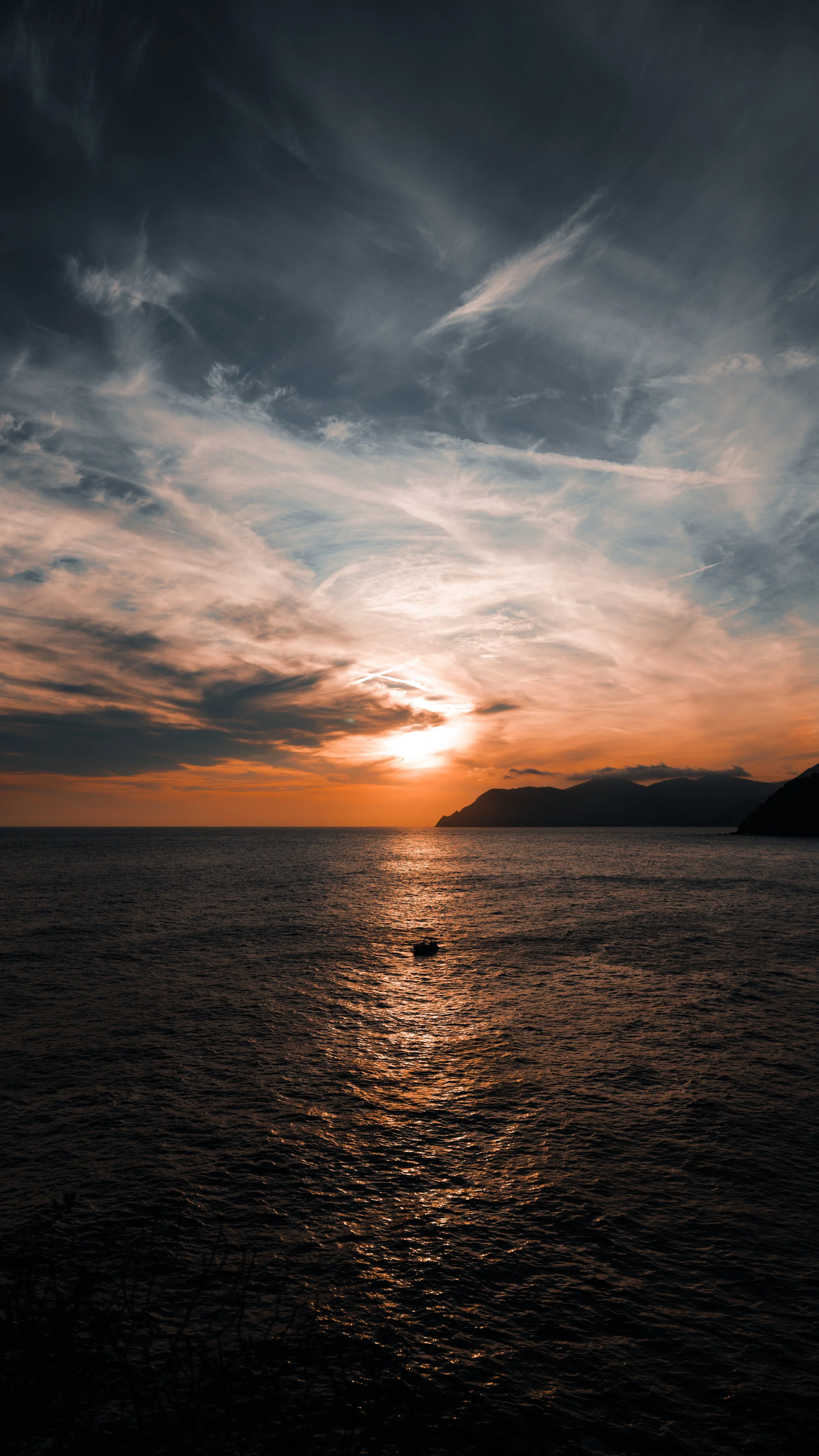 Sonnenuntergang über dem Meer mit Wolken am Himmel und einer kleinen Insel im Wasser.