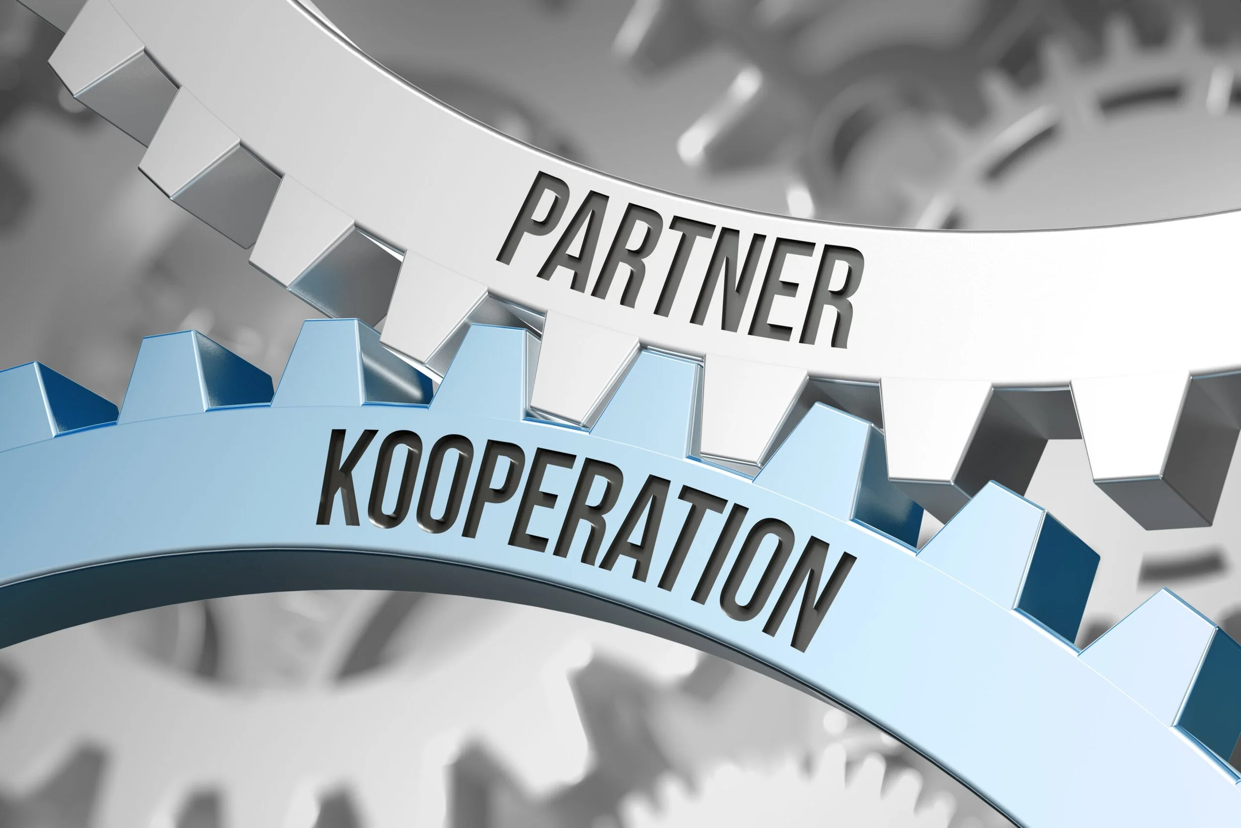Zwei Zahnräder, eines mit dem Wort 'PARTNER' und das andere mit dem Wort 'KOOPERATION', symbolisieren Zusammenarbeit.